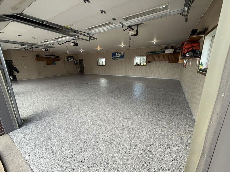 Empty garage with speckled epoxy floor, overhead lights, and storage shelves along the walls