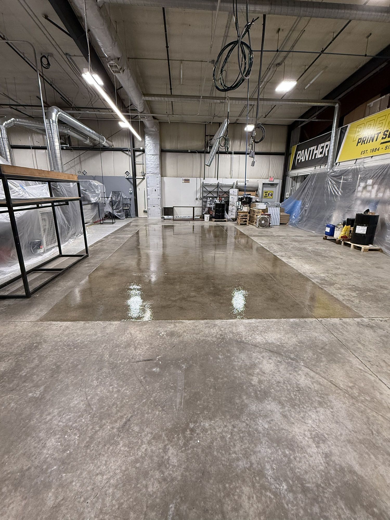 Empty industrial warehouse with wet concrete floor, metal shelving, and overhead lights.