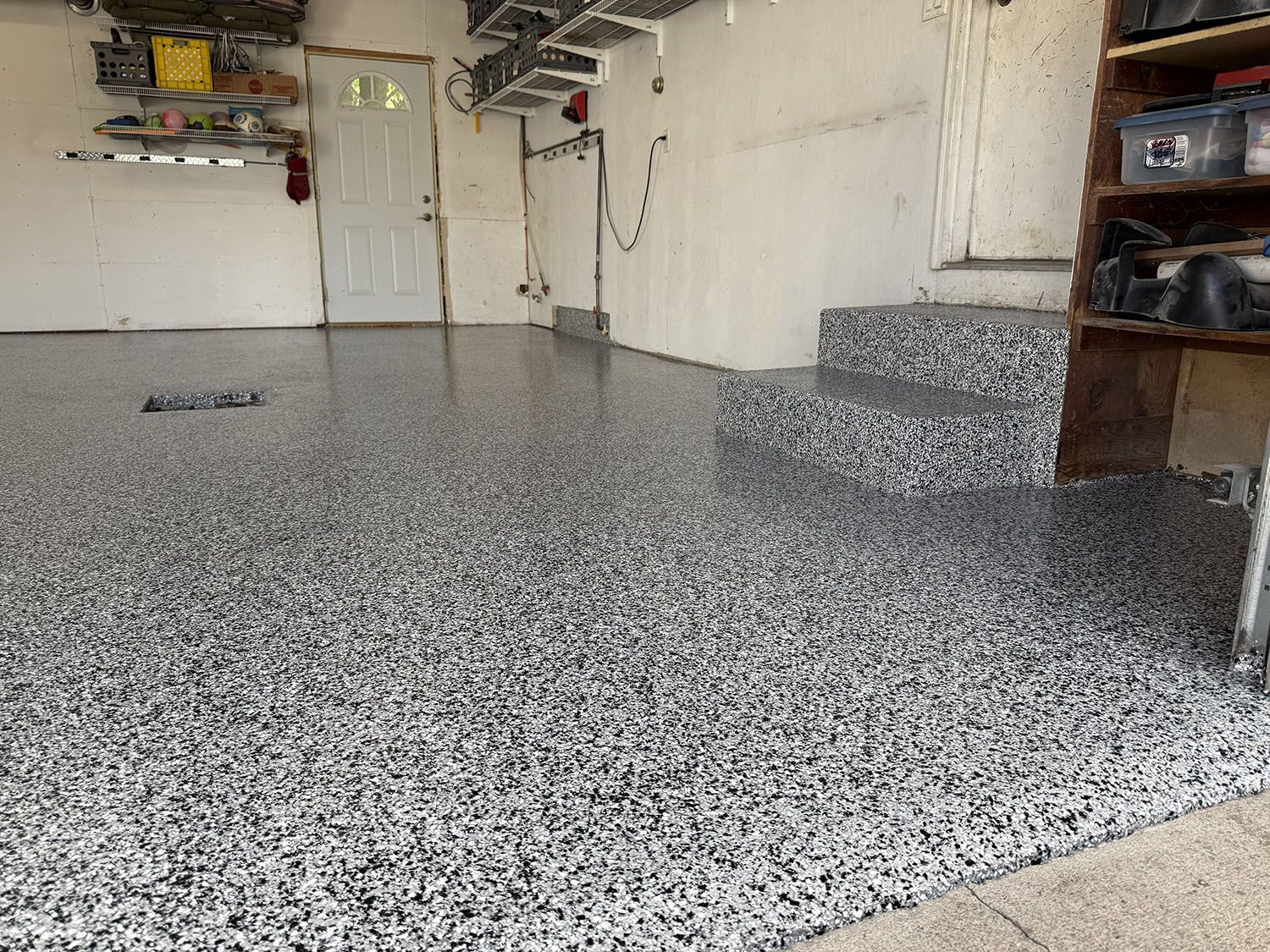 Spacious garage with speckled epoxy floor, white walls, storage shelves, and a workbench corner.