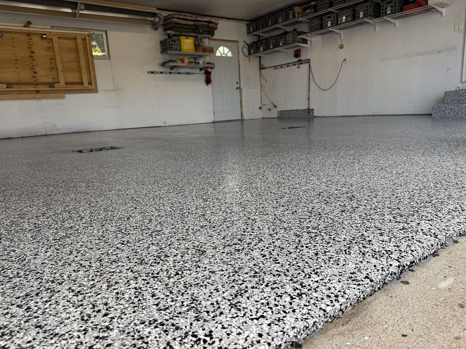 Empty garage with a speckled epoxy floor and wall-mounted storage shelves.
