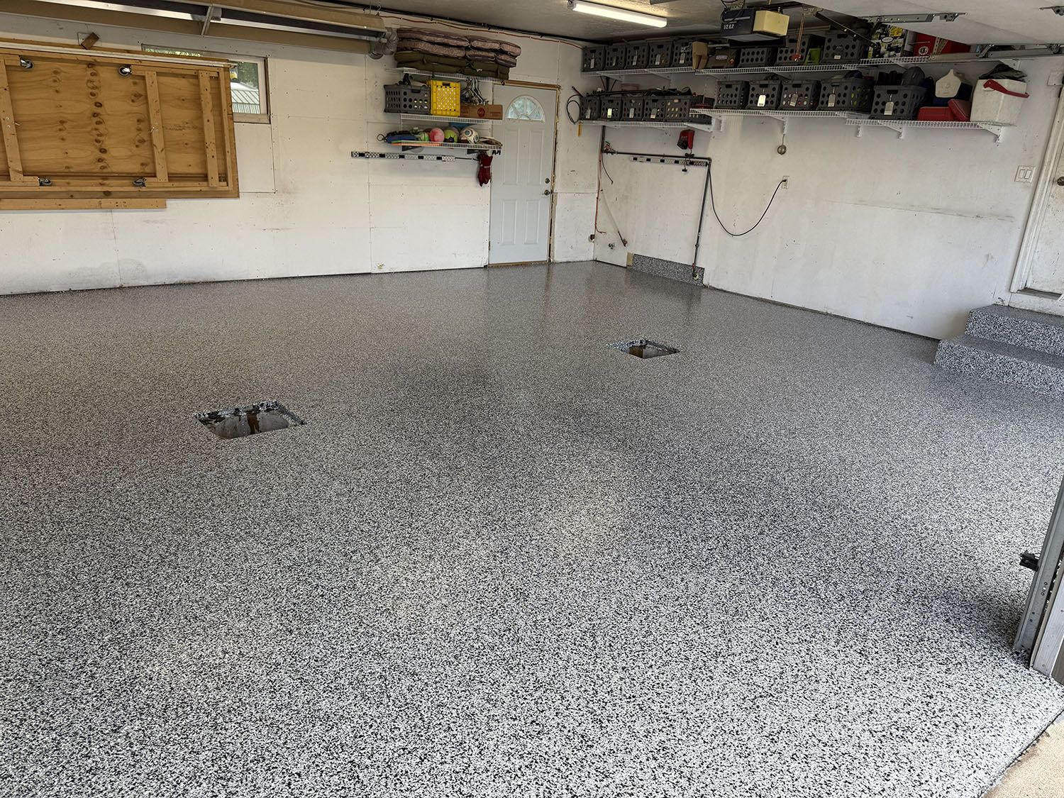 Empty garage with speckled epoxy floor, white walls, and shelves mounted near the ceiling.