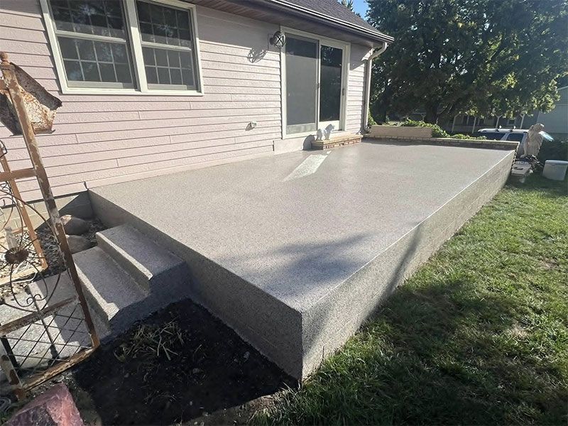 Concrete patio with steps beside a house, extending into a grassy yard.