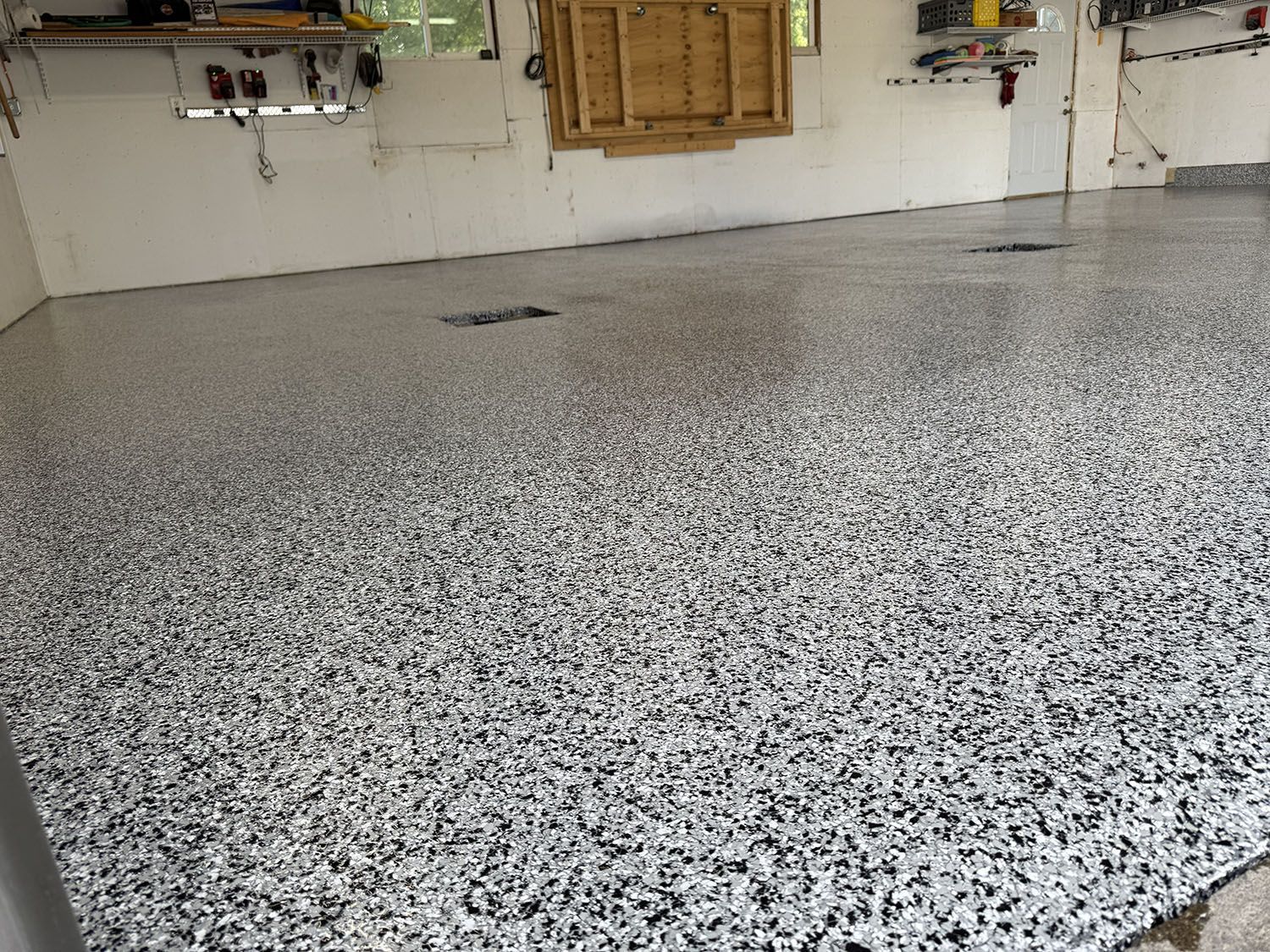 Speckled epoxy garage floor with a white wall and cabinets in the background.