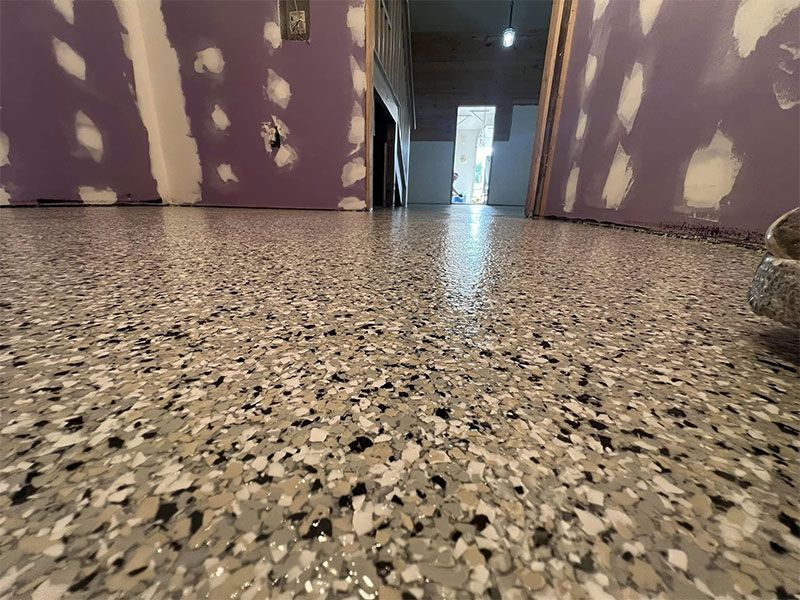 Low-angle view of a hallway with unfinished purple drywall and a speckled terrazzo floor