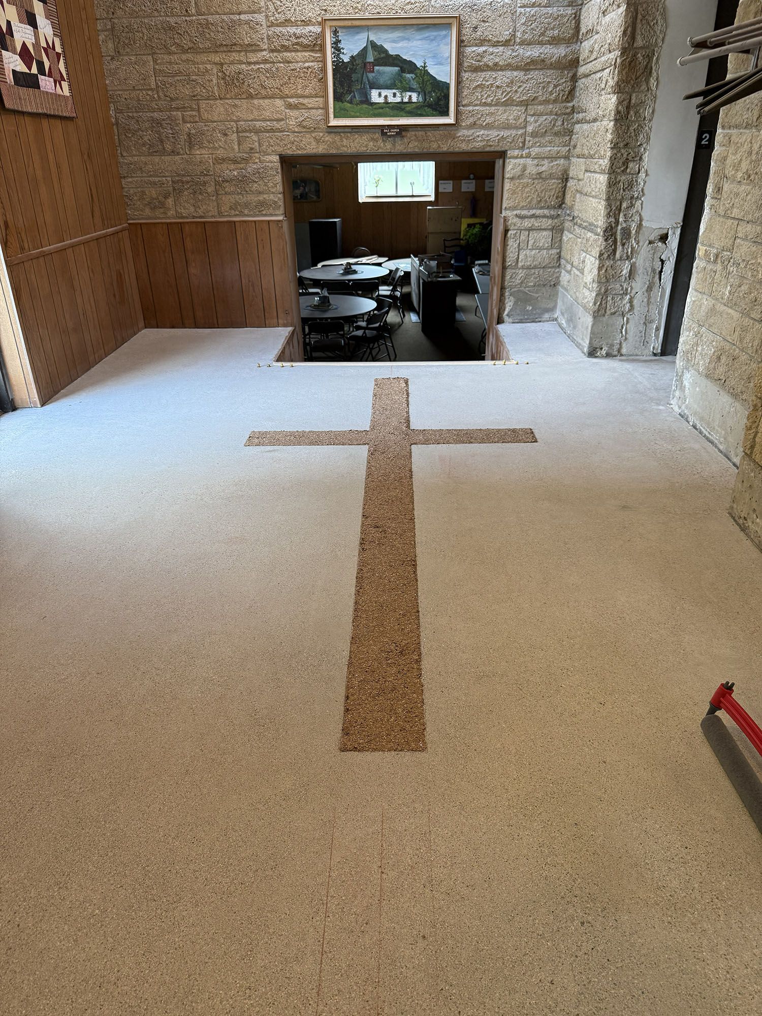 Stone chapel interior with a pebble floor and a cross-shaped inlay leading to an altar room.