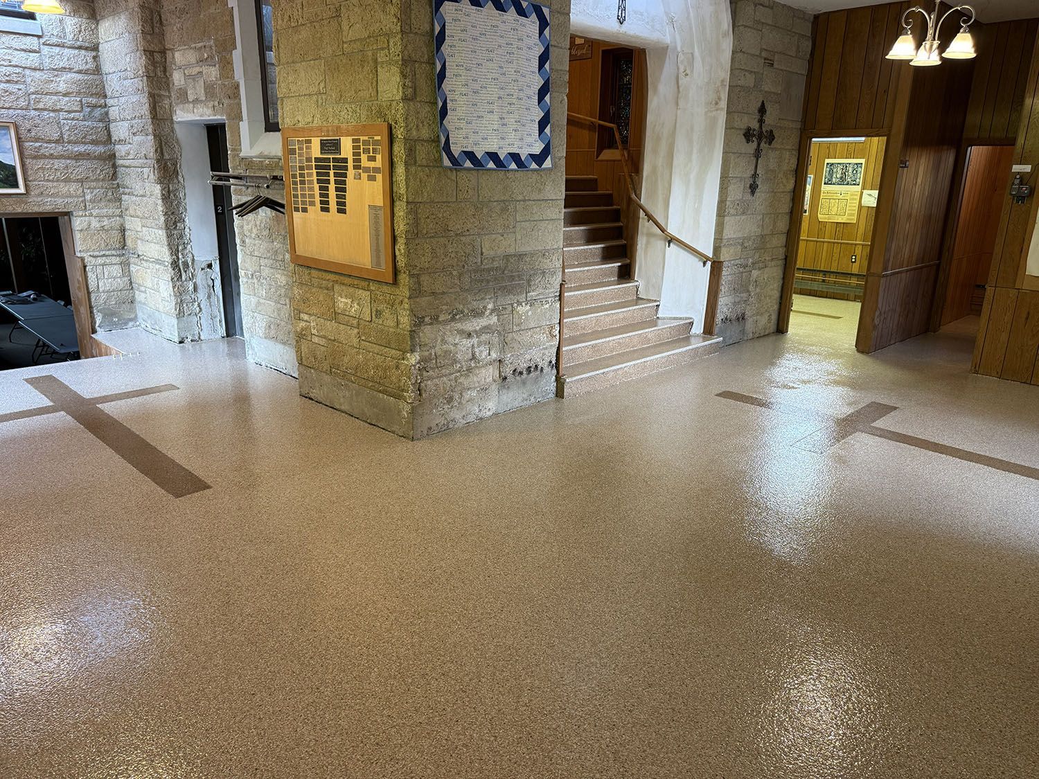 Empty lobby with terrazzo floor, stone walls, wooden stairs, and elevator doors.