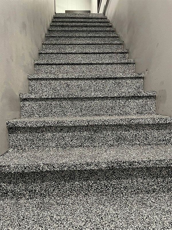 Narrow indoor staircase with gray speckled steps and beige walls, viewed from the bottom up