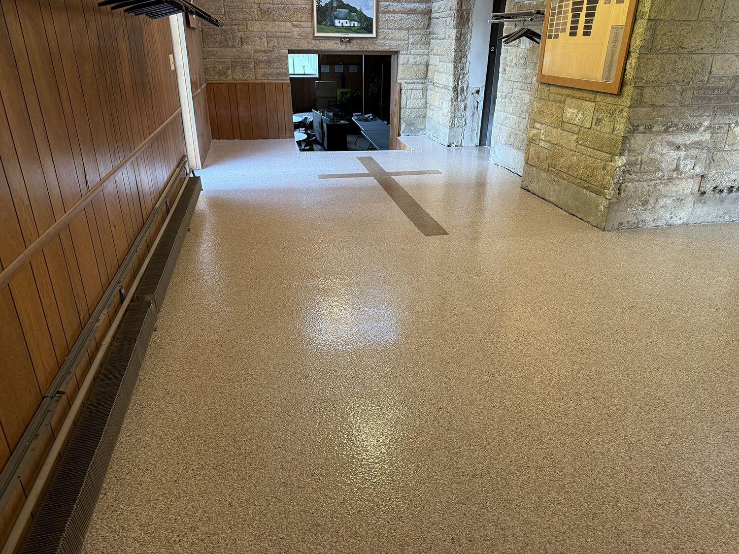 Dim stone hallway with a speckled floor leading to a doorway and wall-mounted frames.