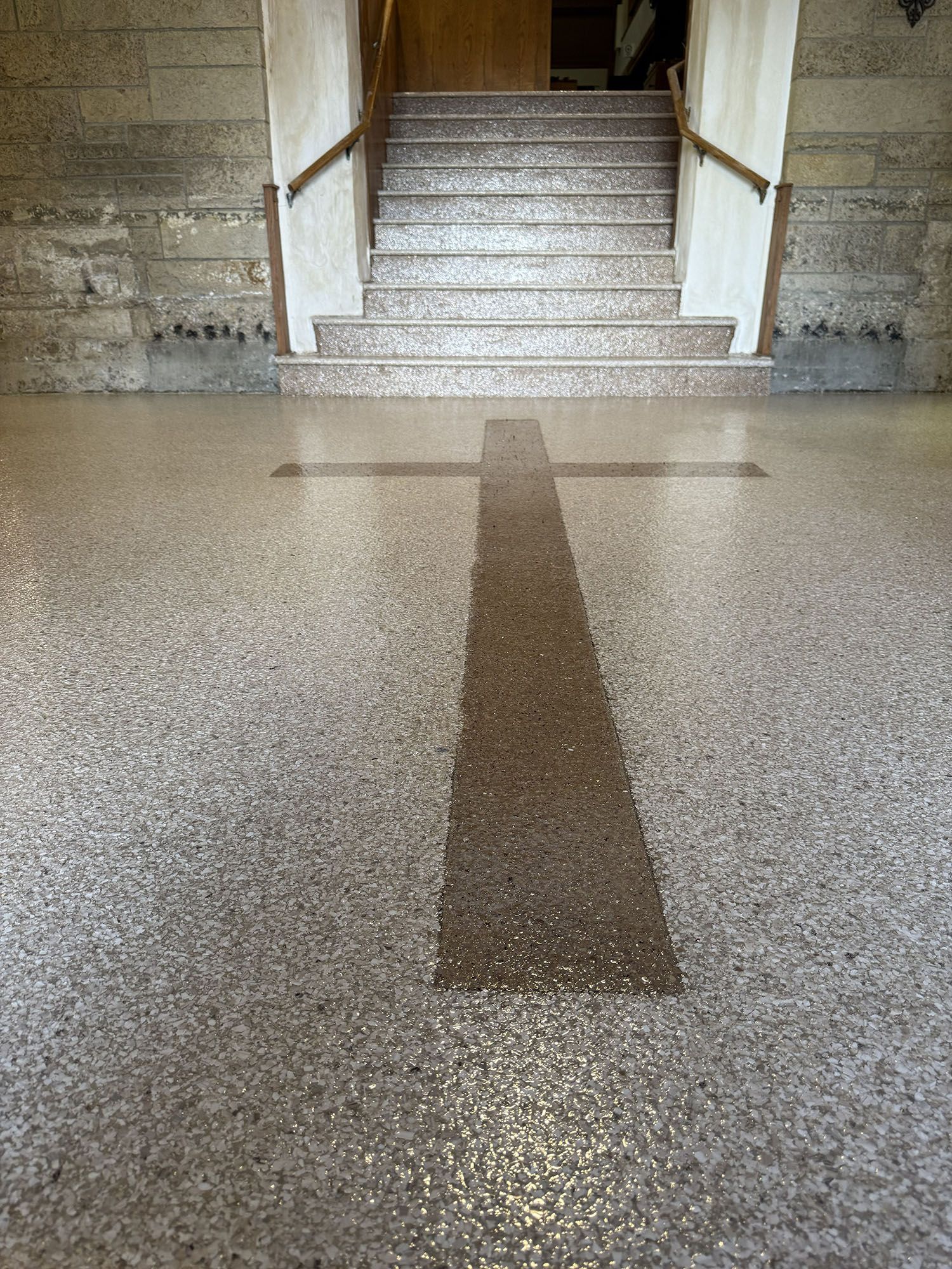 Tiled hallway with a darker center strip leading to a staircase in a stone building.