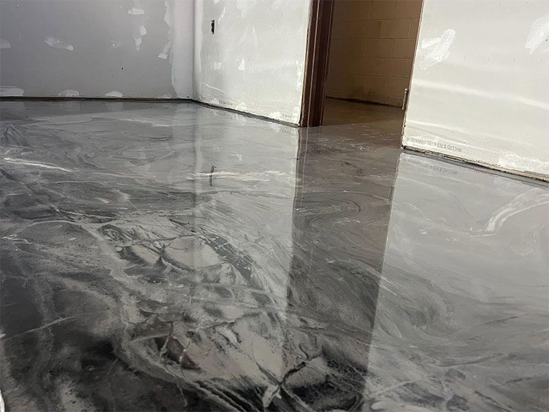 Shiny gray epoxy floor in an empty room, with reflective walls and doorway.