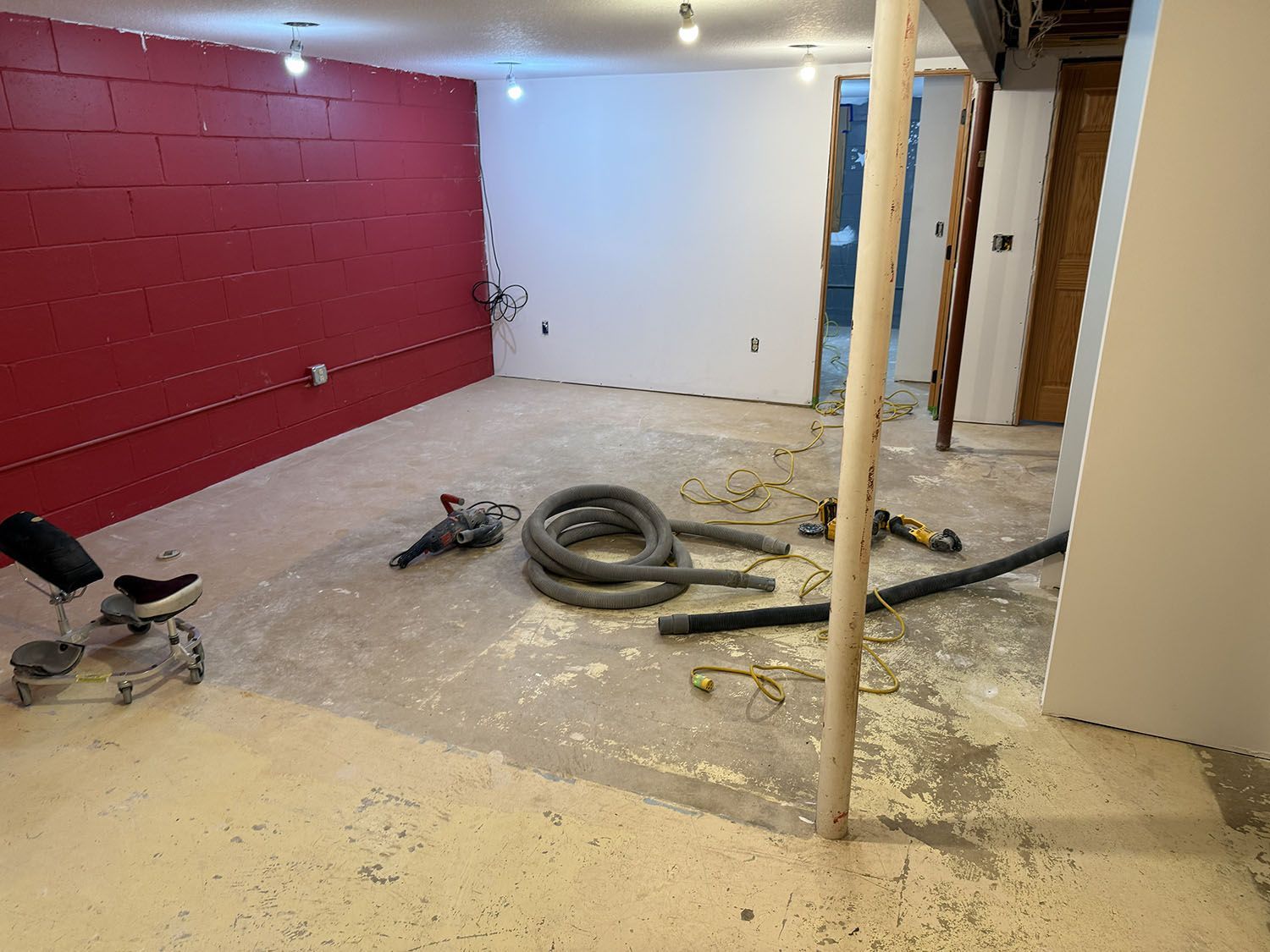 Partially renovated room with red and white walls, exposed pipes, tools, and construction debris on the floor.
