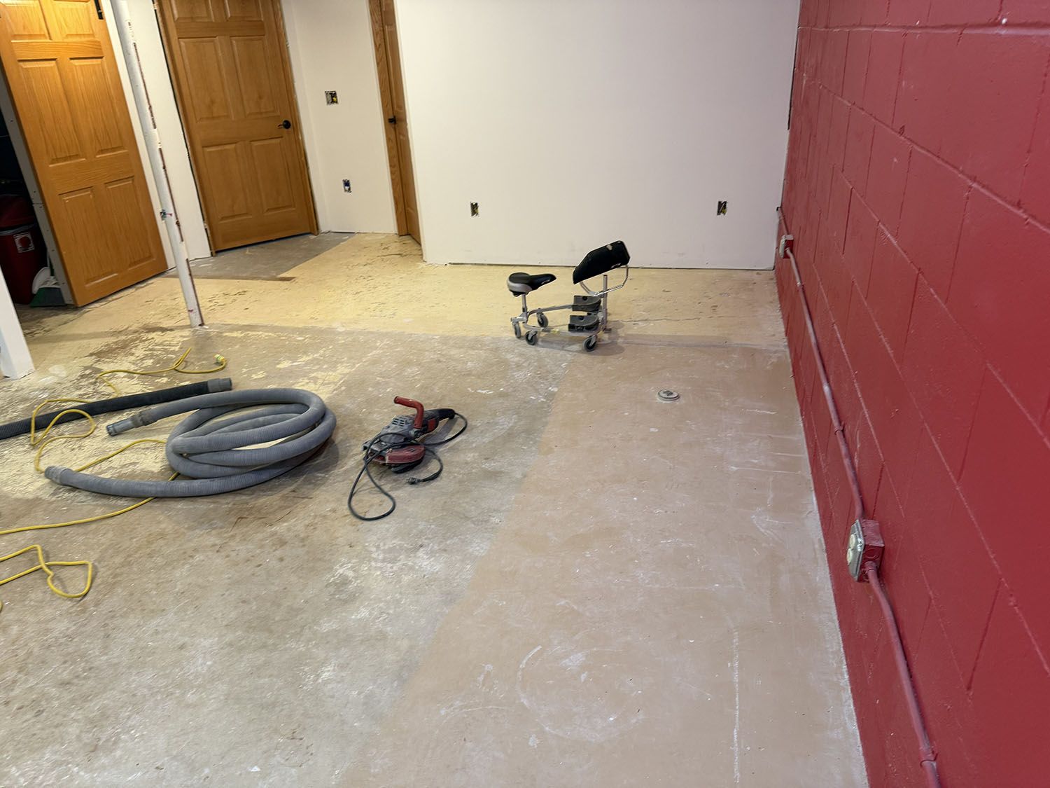 Partially renovated room with tools, coiled hose, and dust on the floor near closed wooden doors.