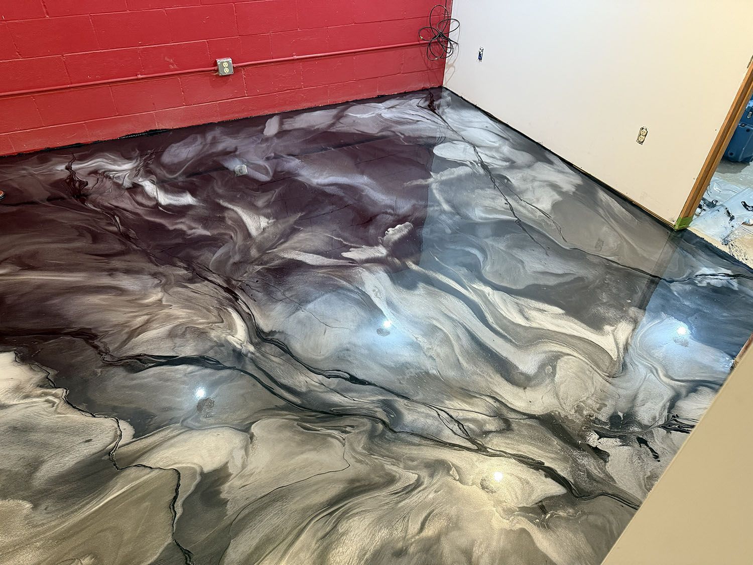 Swirled black, gray, and white epoxy floor in a room with a red wall and beige door frame.