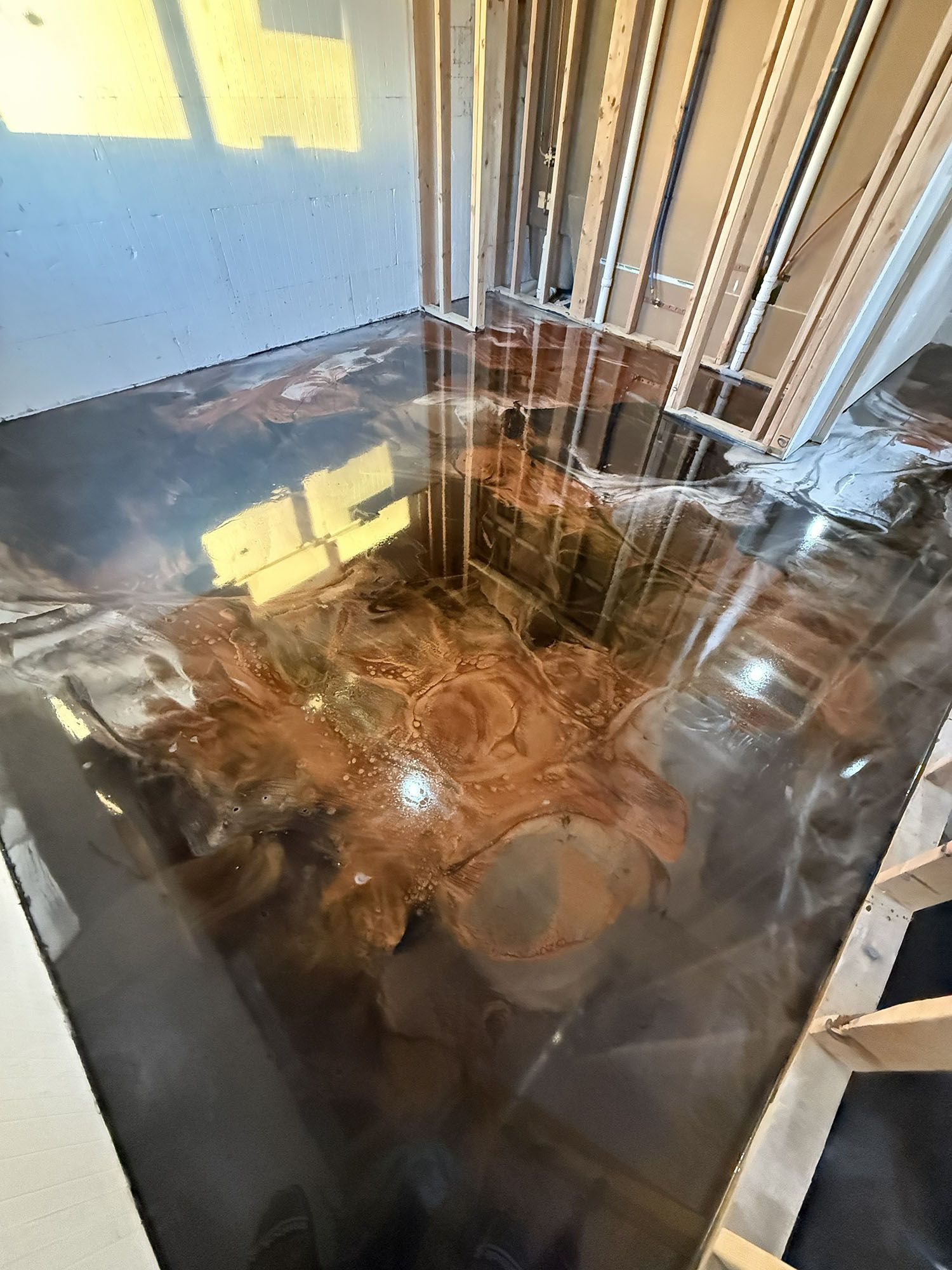 Flooded indoor room with standing water, reflecting windows and exposed pipes.