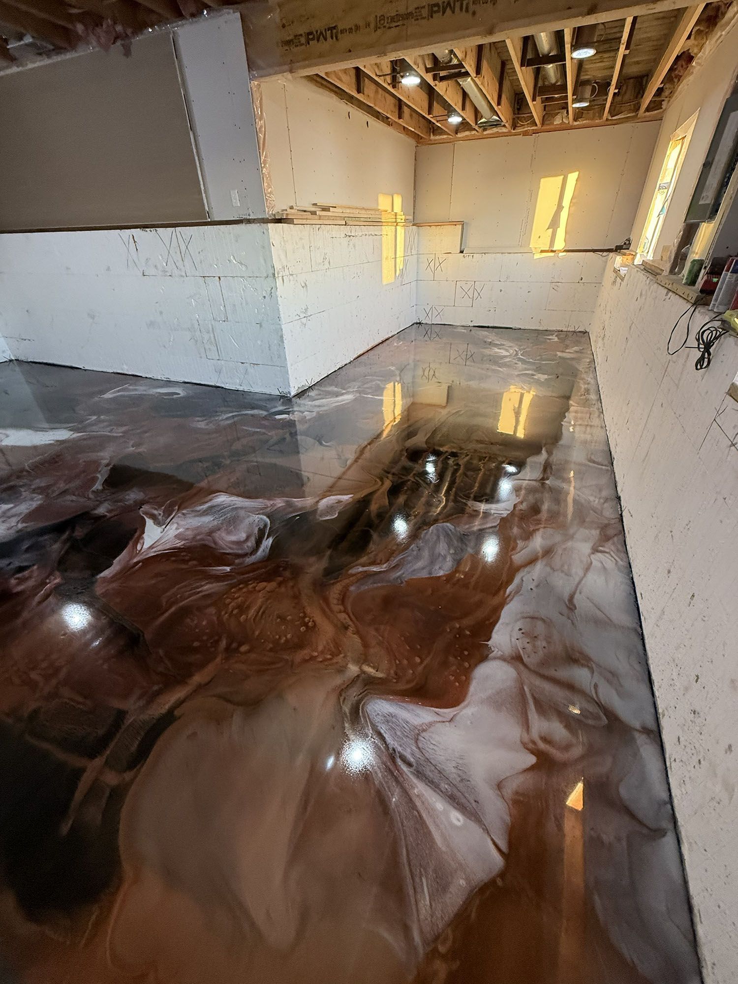 Flooded unfinished room with glossy water covering the floor and exposed ceiling beams overhead.