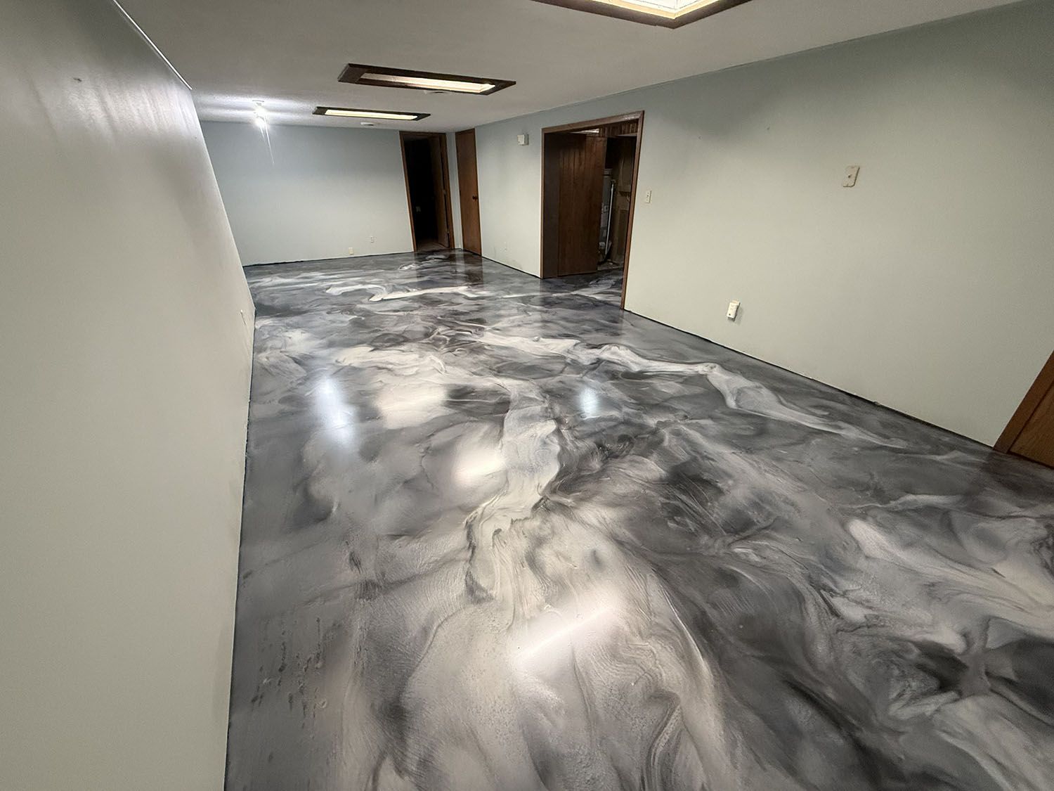Empty hallway with marbled gray floor and white walls, lit by ceiling lights.