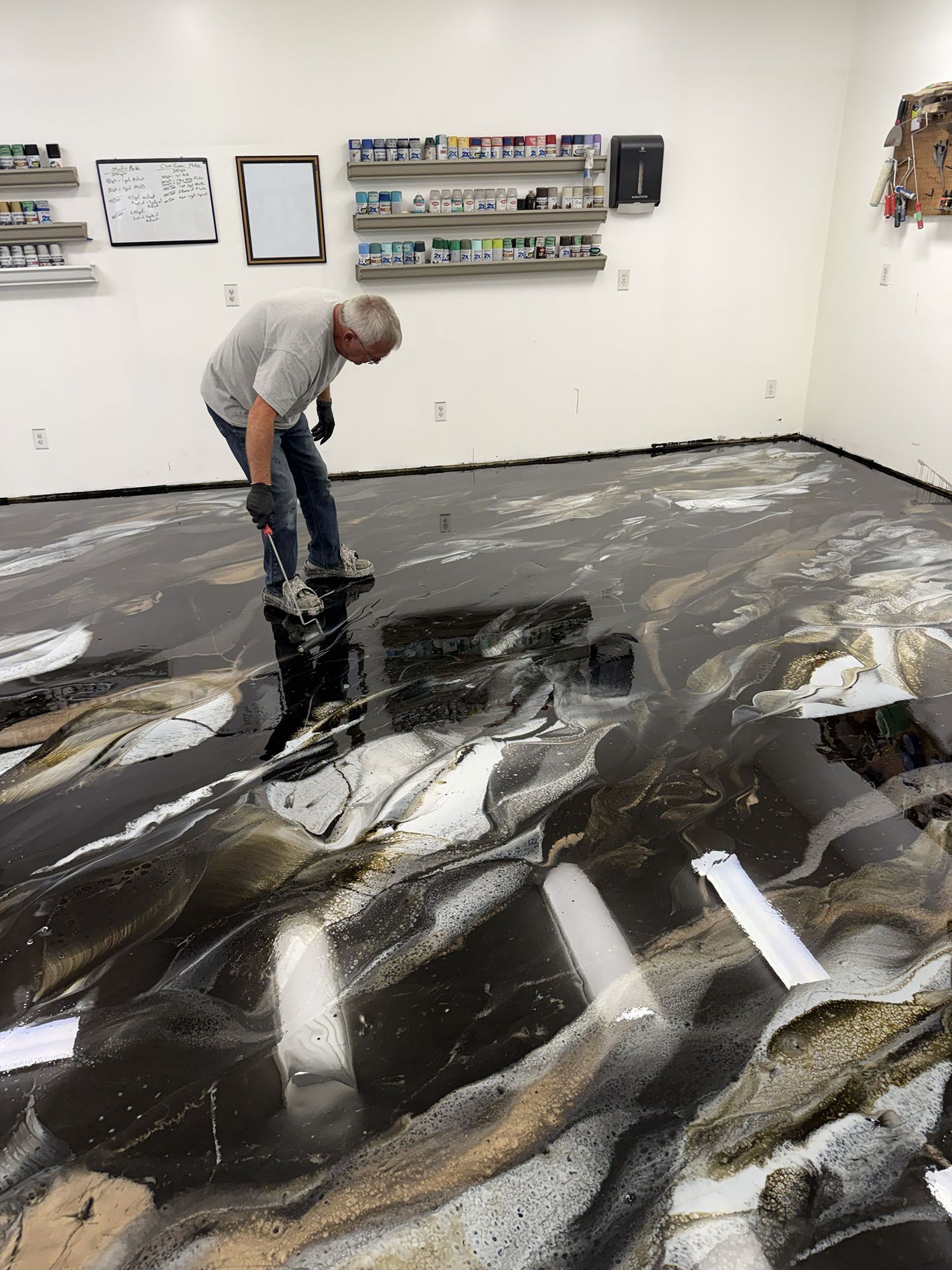 Person using a roller to spread black-and-white paint across a gallery floor.