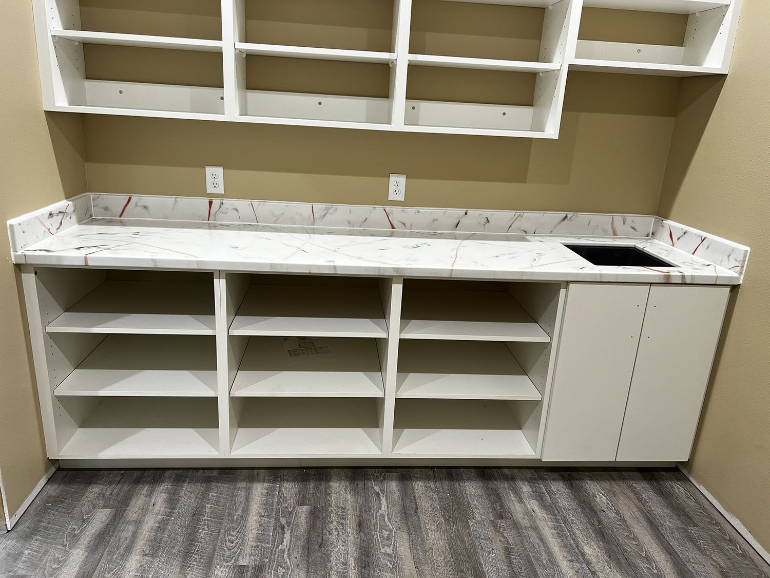 Built-in white cabinets with marble countertop and open shelving in a room with tan walls and gray carpet.
