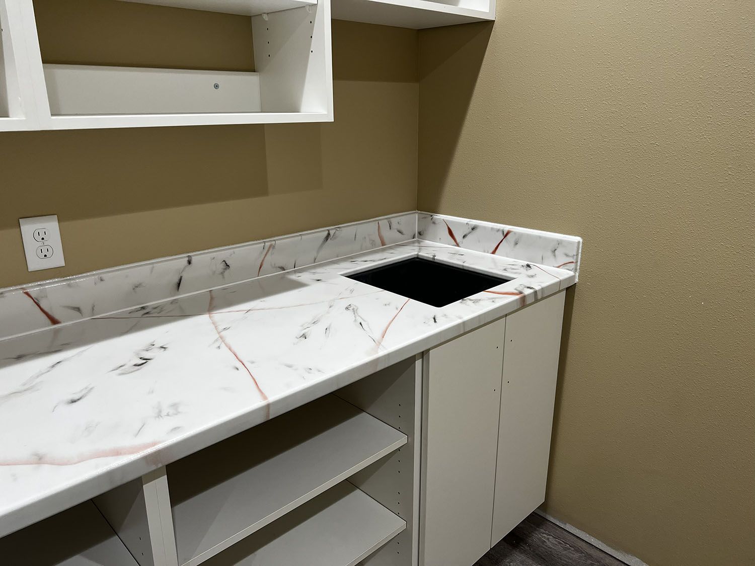 Empty laundry room with white cabinets, marble-look countertop, and black sink on beige walls.