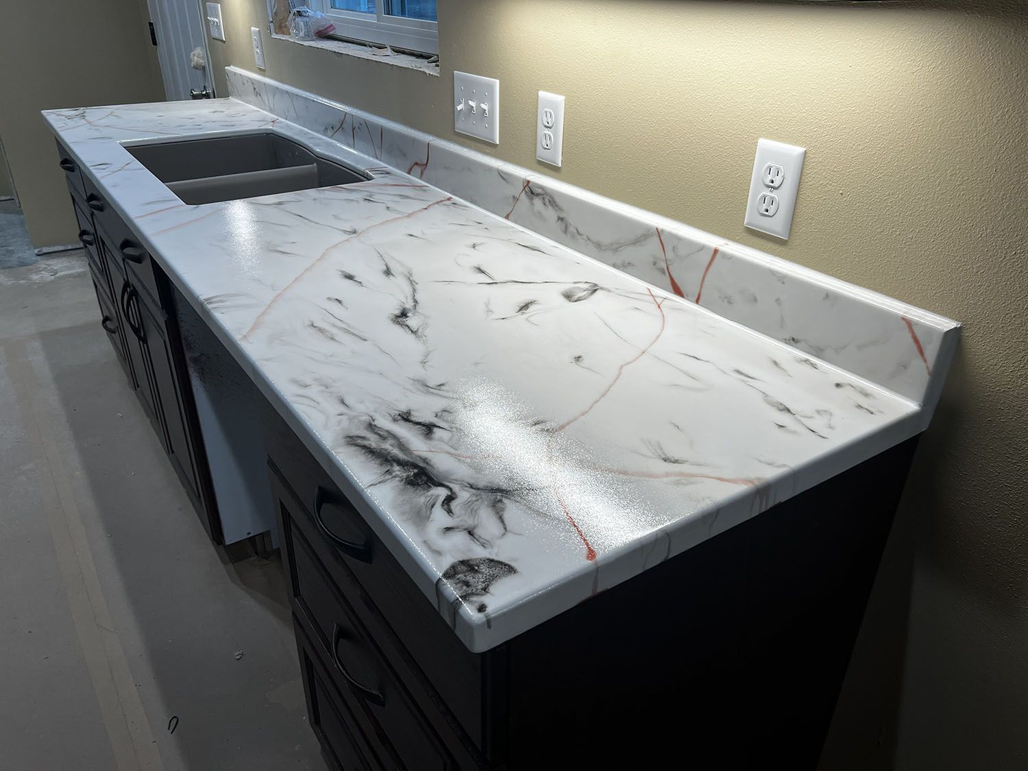 Marble-look kitchen countertop with sink cutout, black cabinets, and wall outlets in a modern kitchen.