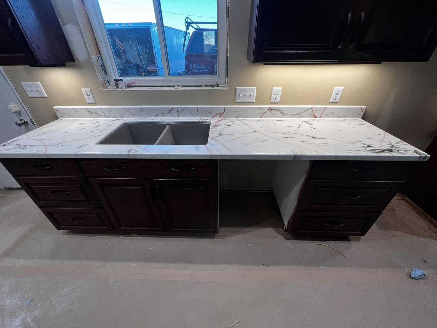 Kitchen island with white speckled countertop, double sink, and dark wood cabinets in a new room.
