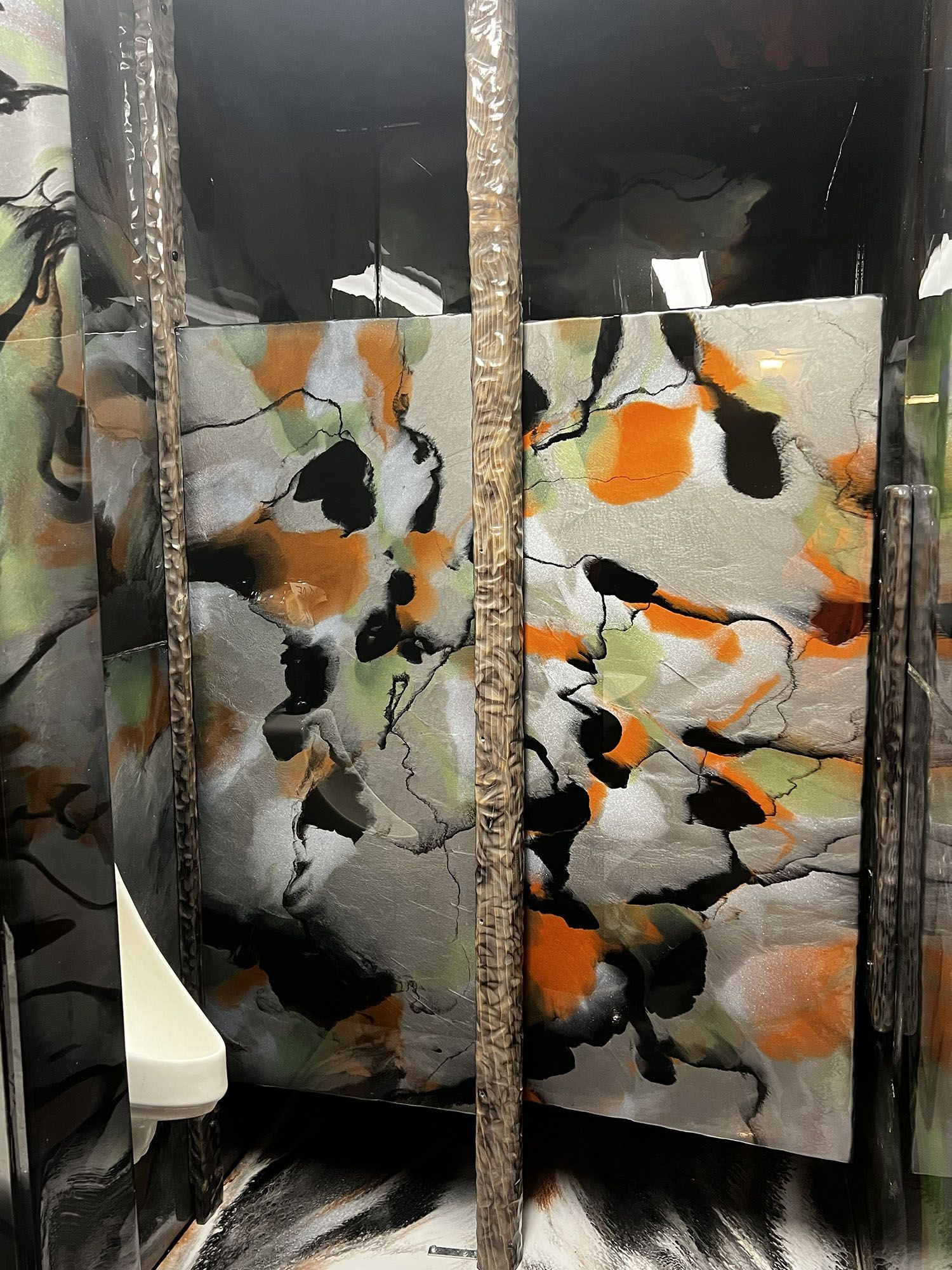 Abstract painting with orange, black, white, and gray shapes behind vertical metal bars.