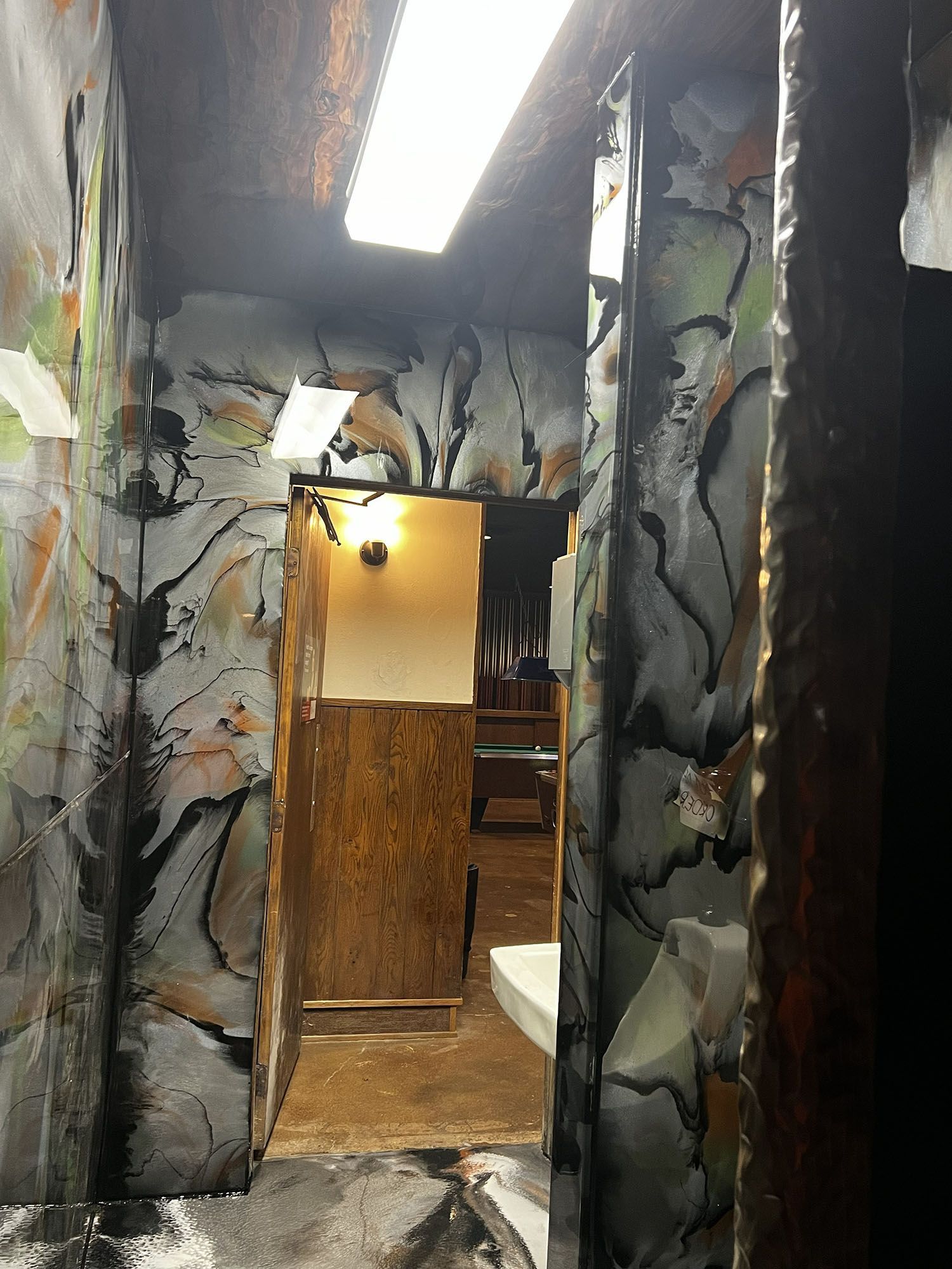 Narrow hallway with dark abstract mural walls, bright ceiling light, and an open doorway ahead.