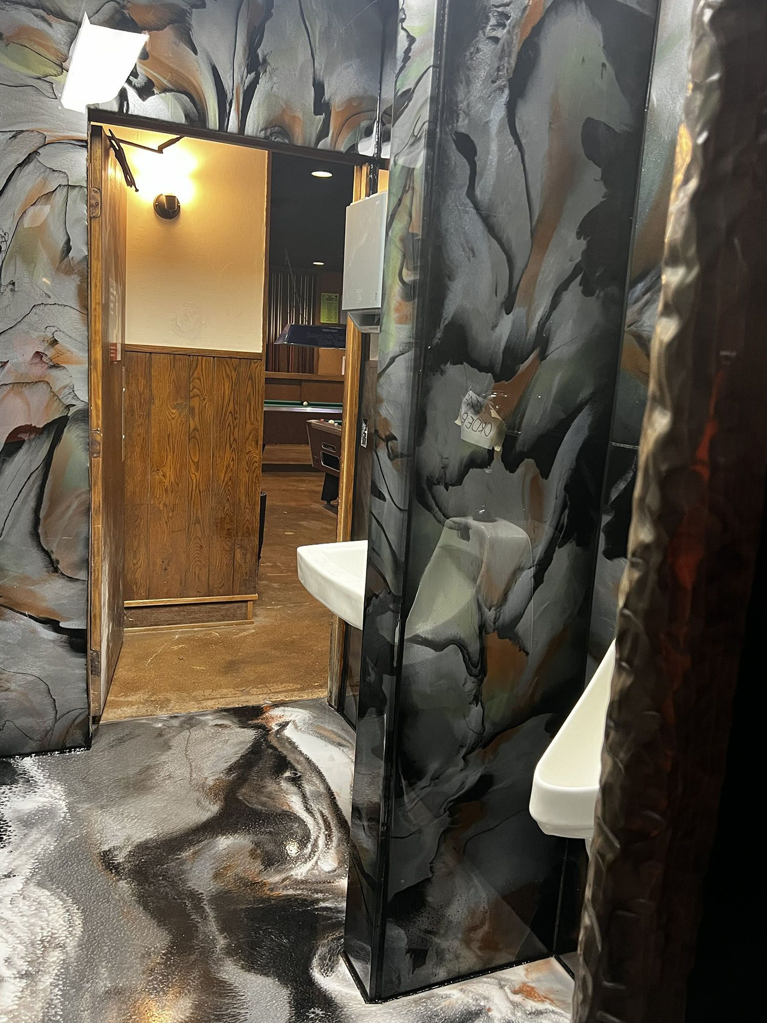 Narrow hallway with torn black-and-gray wall coverings and a doorway to a lit room beyond.