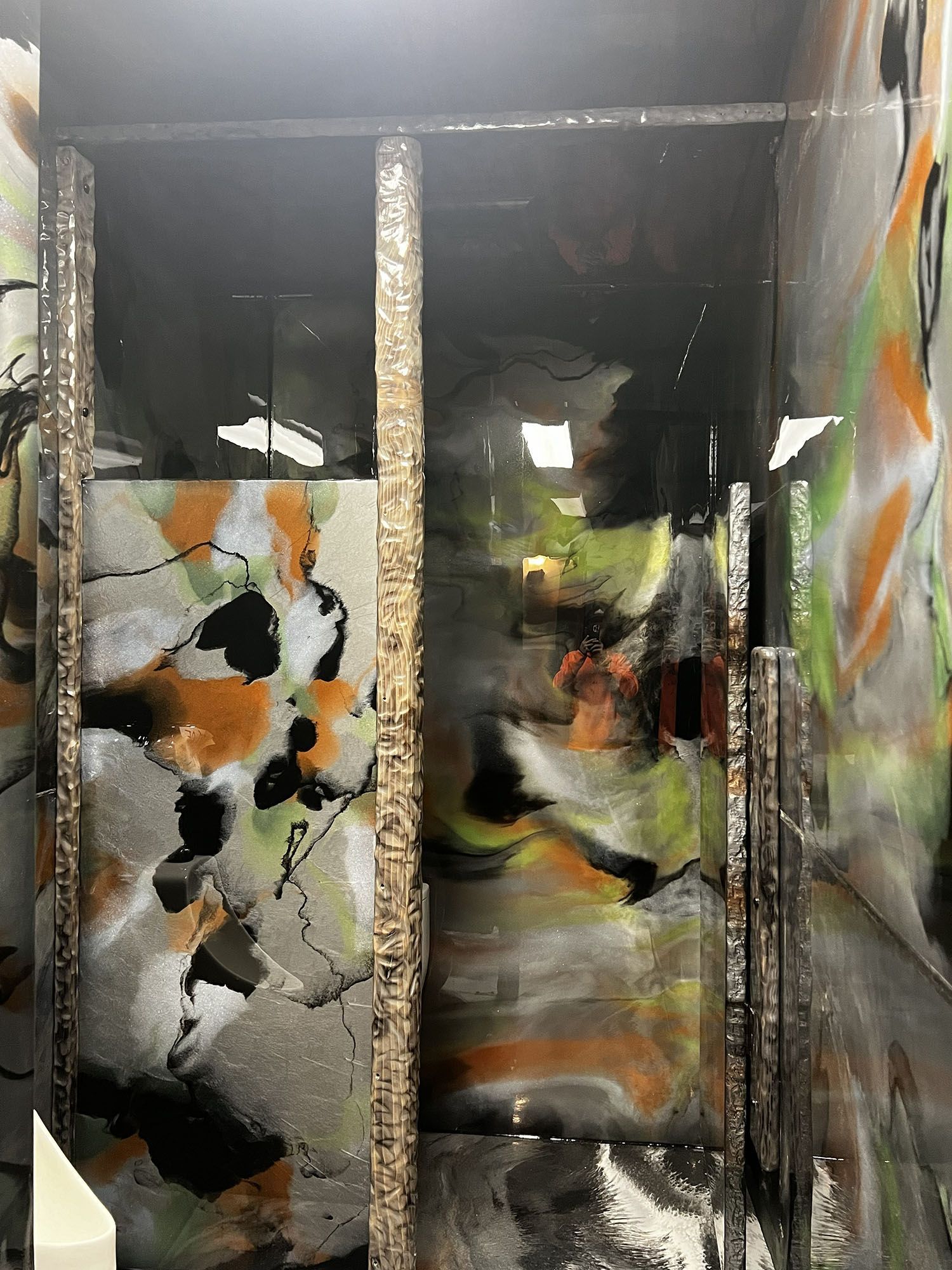 Abstract painted corridor with black, orange, and white patterns, viewed through glass panels.