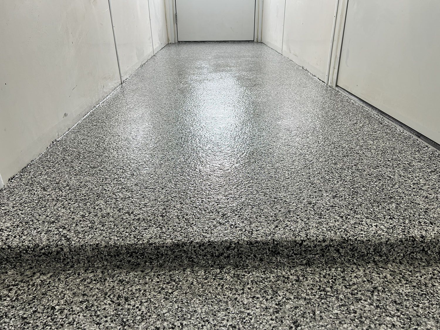 Speckled epoxy floor in a narrow hallway with white walls and closed doors.