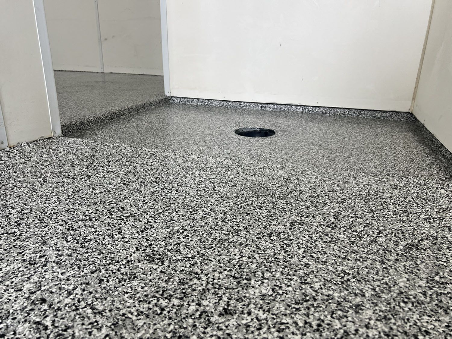 Small empty room with speckled gray floor, white walls, and a floor drain near the back.