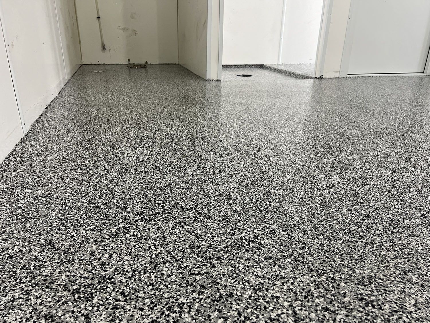 Speckled gray epoxy floor in a white hallway with doors and a small opening in the back wall.