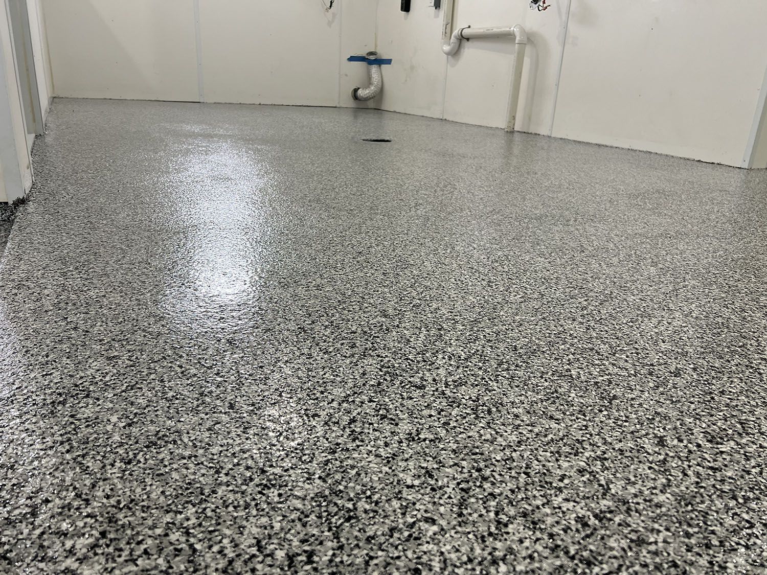 Empty room with glossy speckled epoxy floor and wall-mounted pipes in the back.