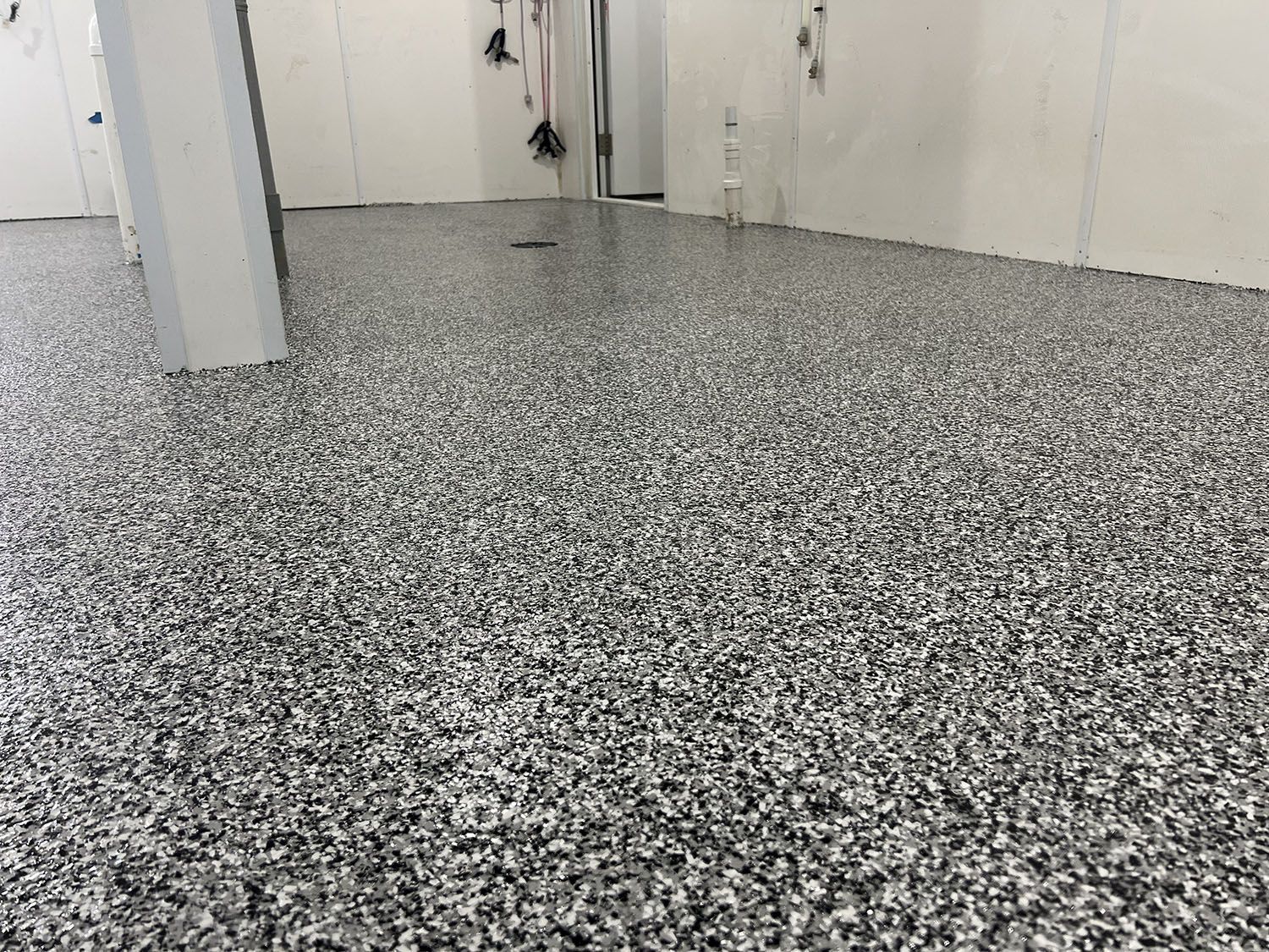 Black-and-white speckled epoxy floor in a white hallway or room, with doors along the walls.
