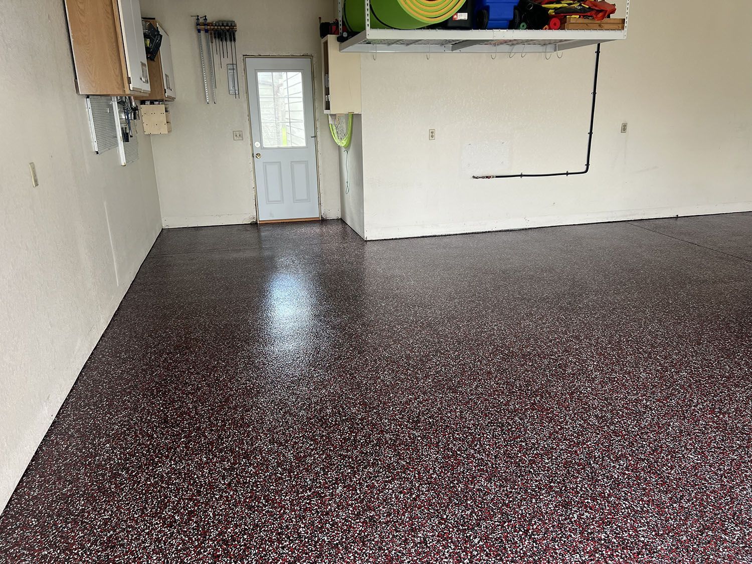 Empty garage with speckled epoxy floor, white walls, and a door at the back.