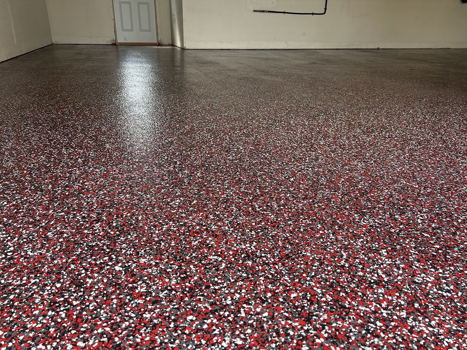 Empty room with red-speckled epoxy floor and white walls, viewed from low angle.