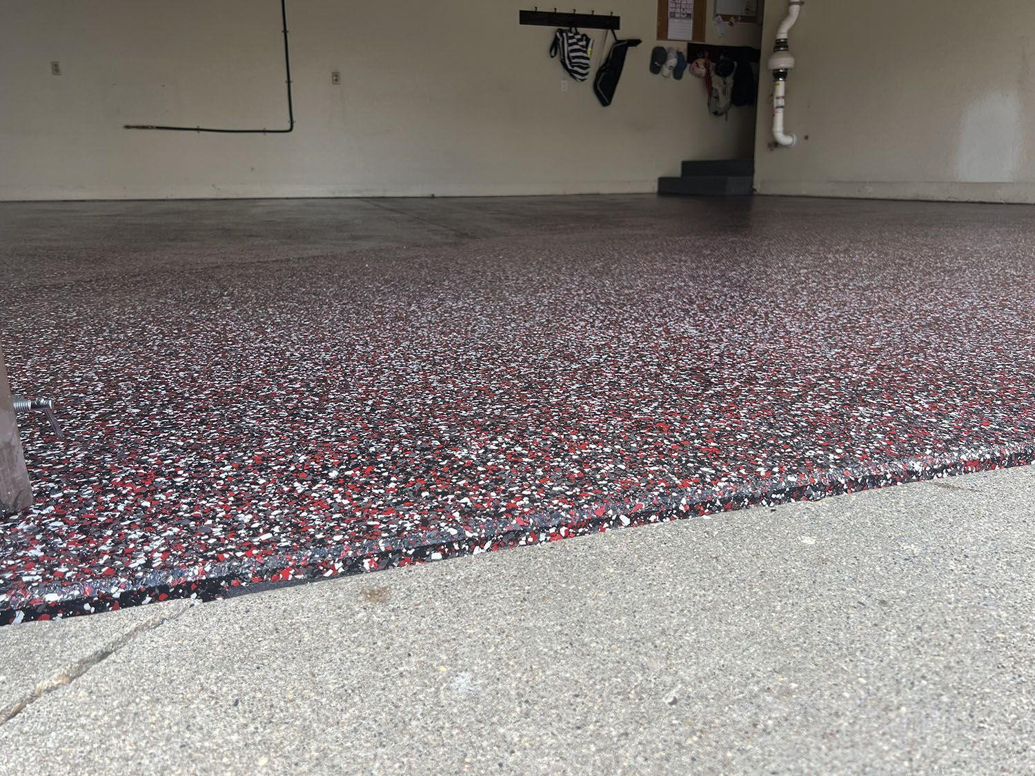 Speckled red and gray carpet in an indoor room with a concrete floor edge and wall-mounted equipment.