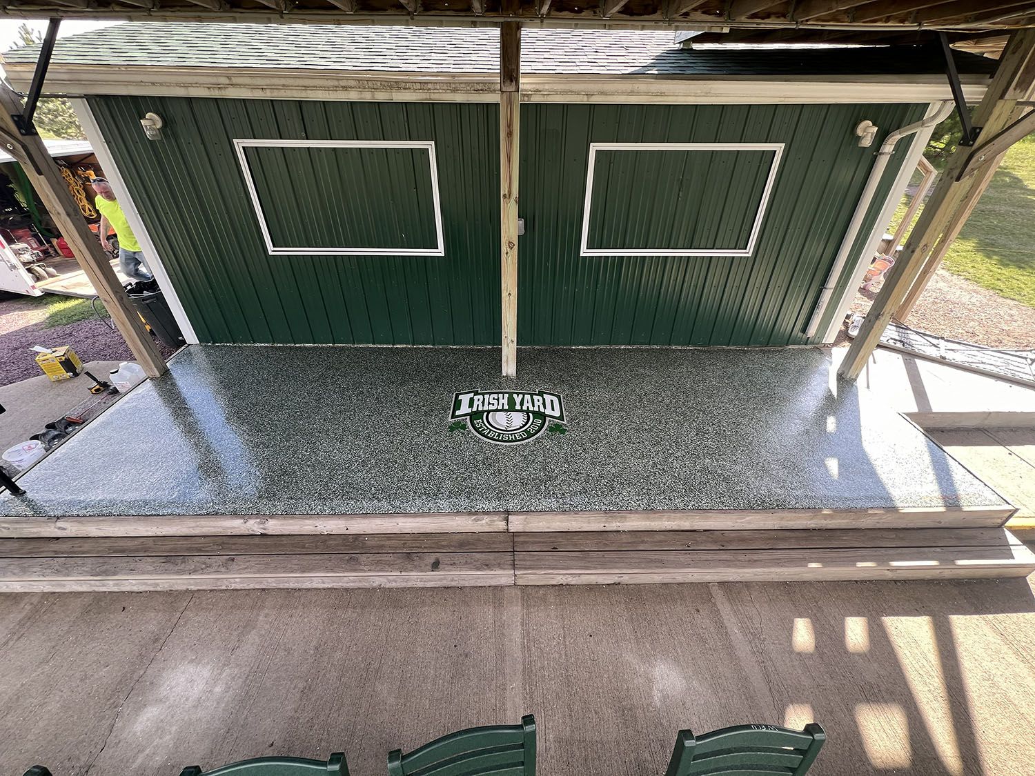 Overhead view of a green shed with white-trimmed windows and a covered gravel patio below.