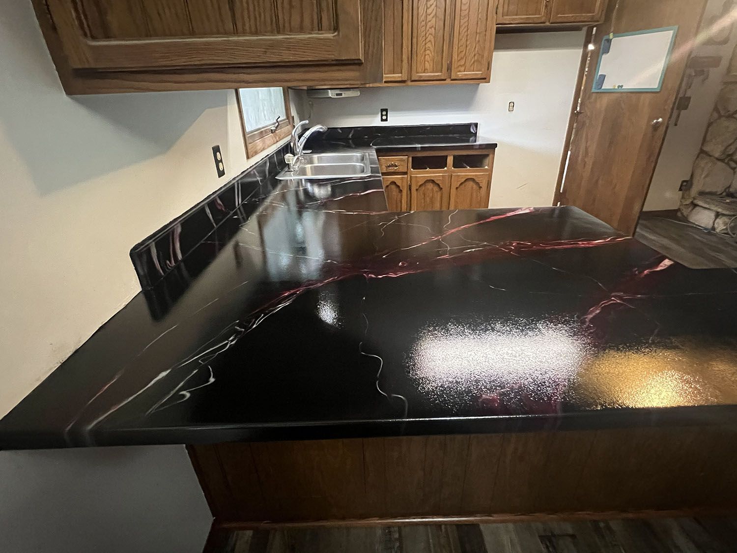 Kitchen with glossy black countertops, wood cabinets, and a tiled backsplash under renovation.