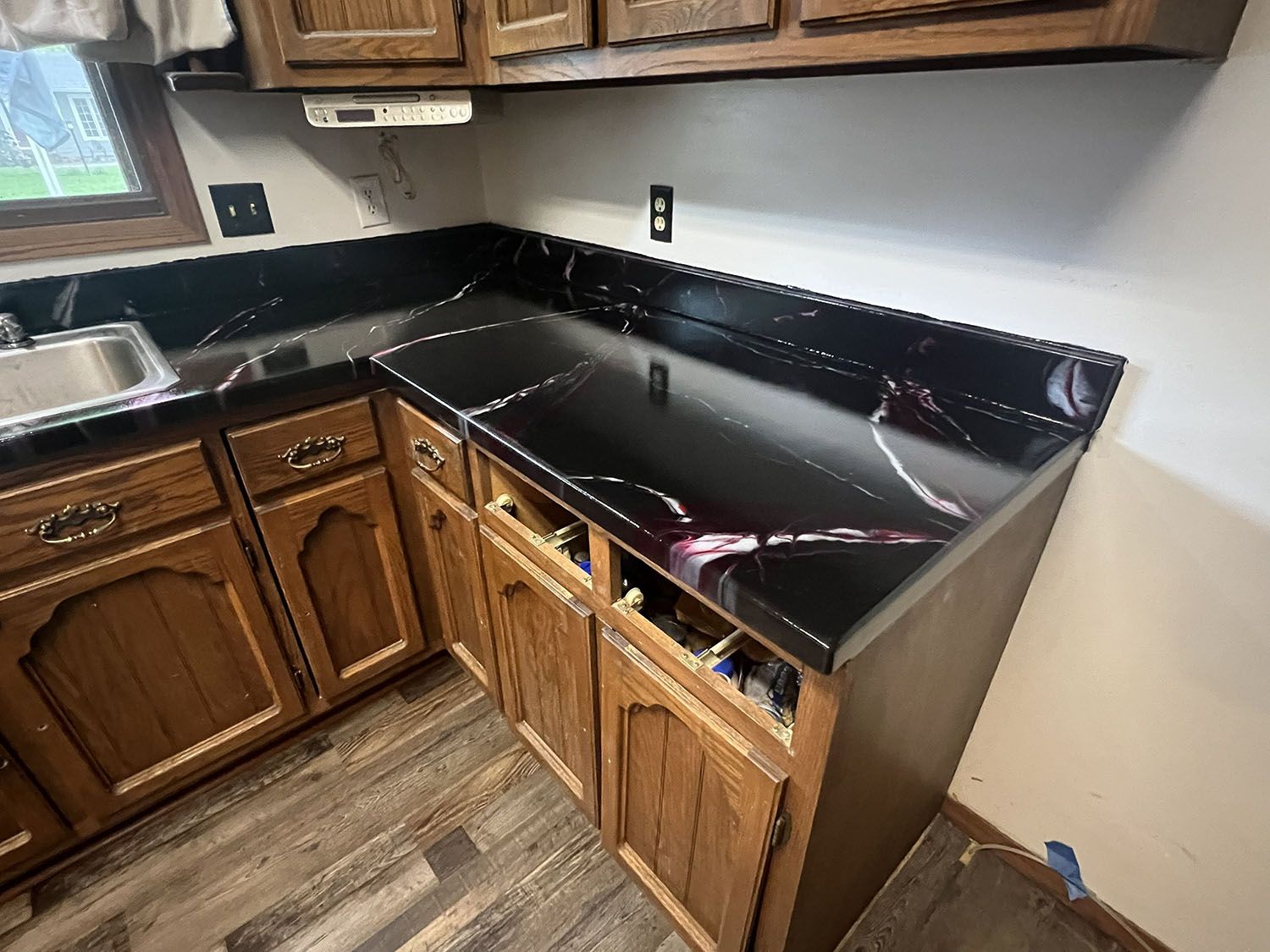 Black granite kitchen countertop and sink with wooden cabinets in a corner kitchen.