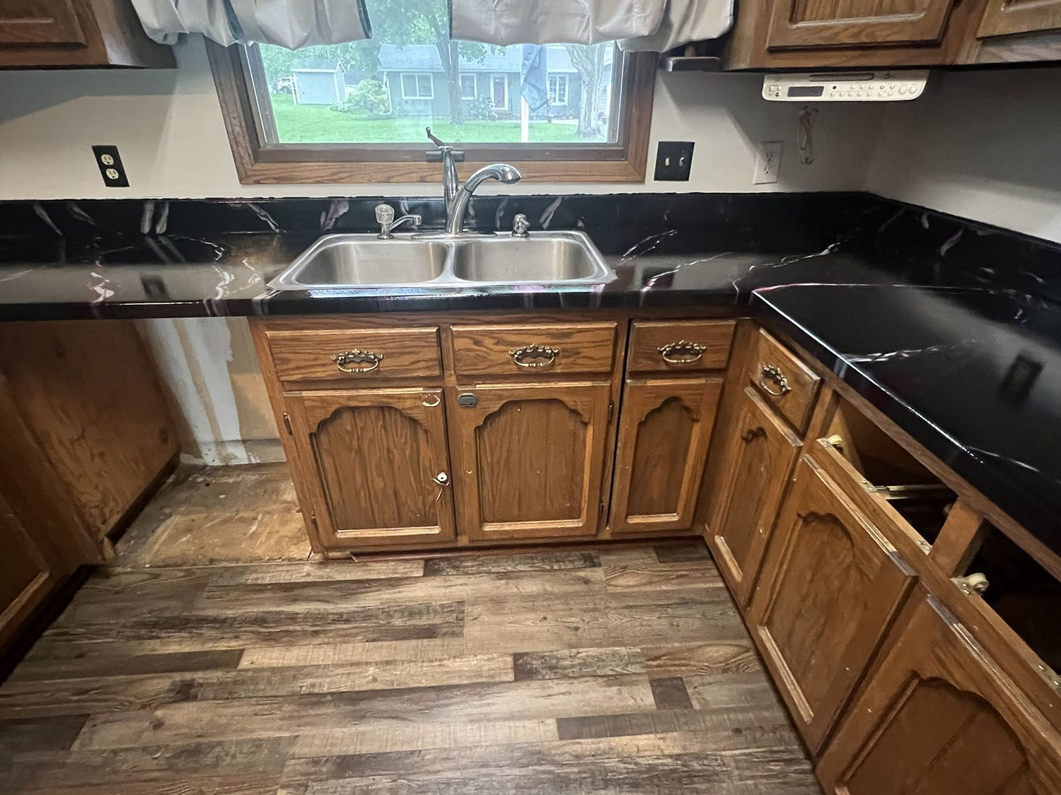 Wooden kitchen with black countertops, farmhouse sink, and wood-look floor beneath a window.