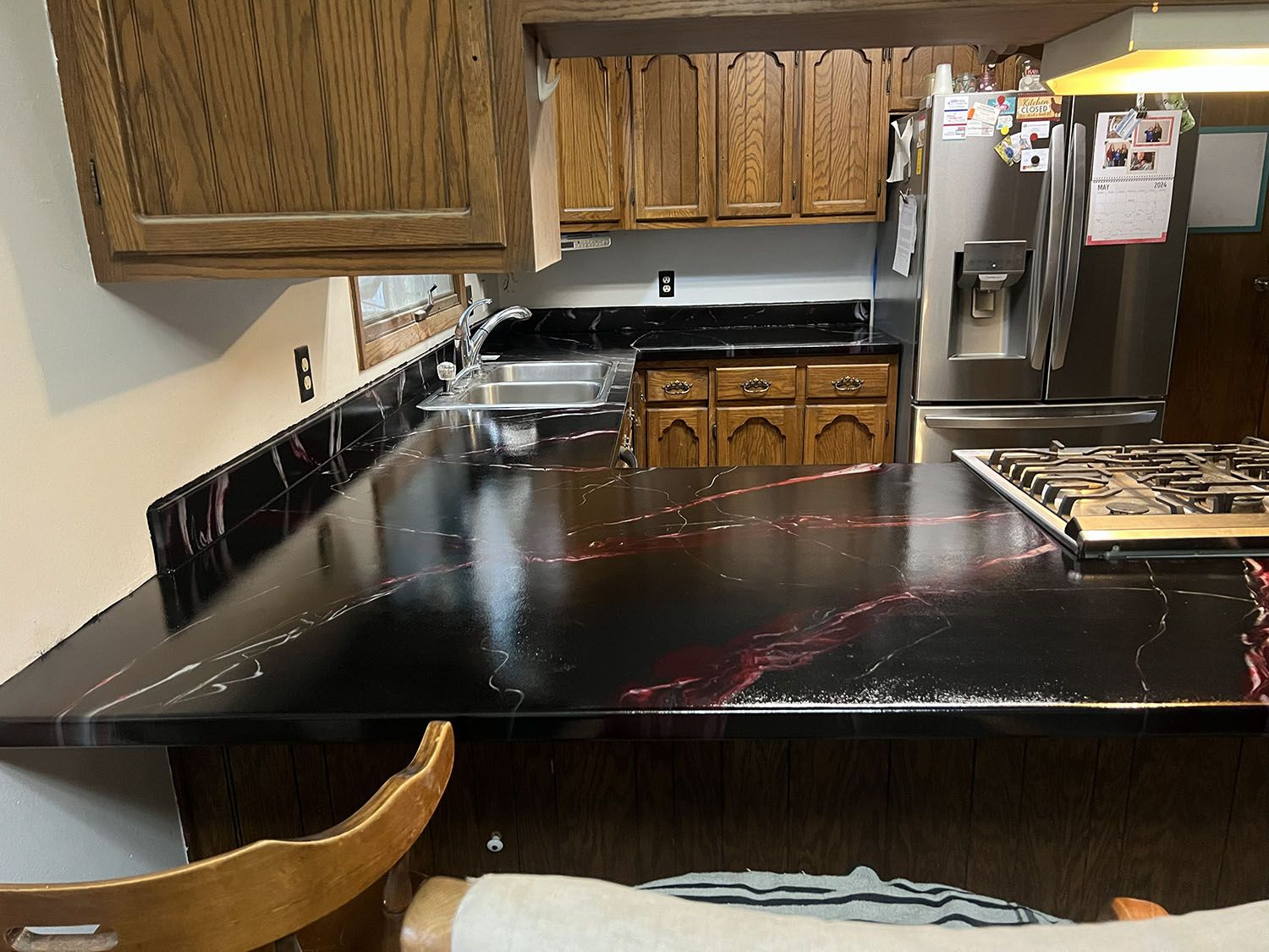 Kitchen with wood cabinets, black countertops, stainless fridge, and a large dark island in the foreground.