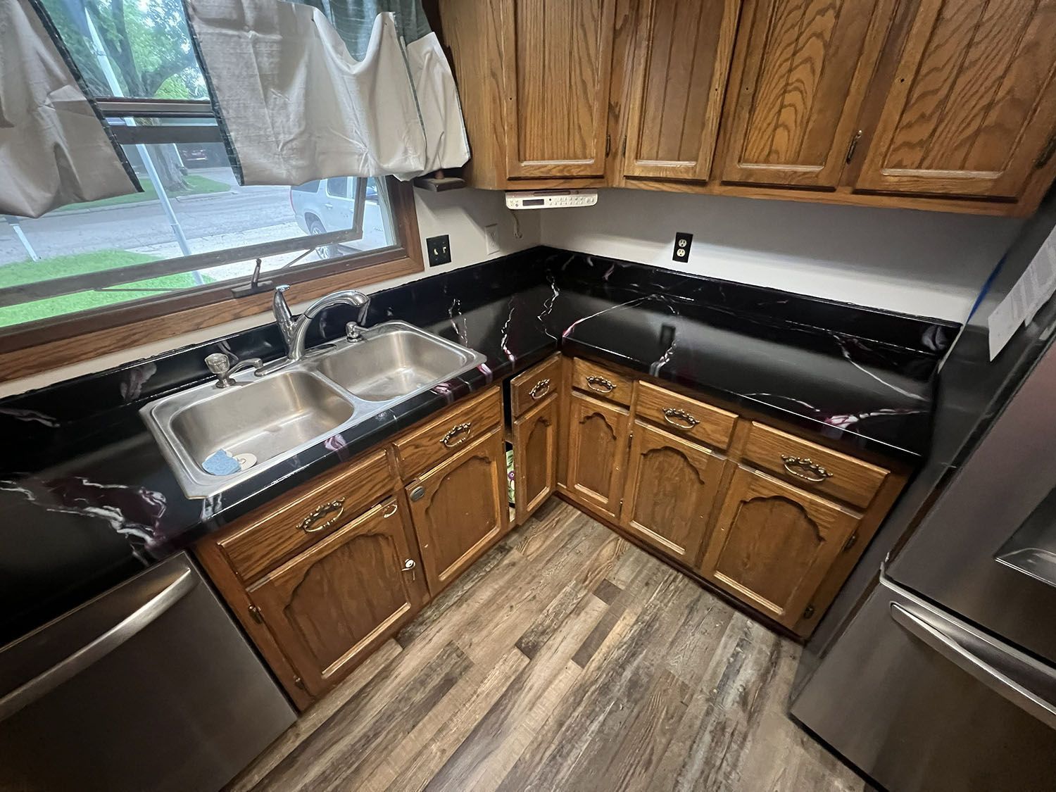 Small kitchen corner with black countertops, wood cabinets, sink by window, and stainless steel appliances.