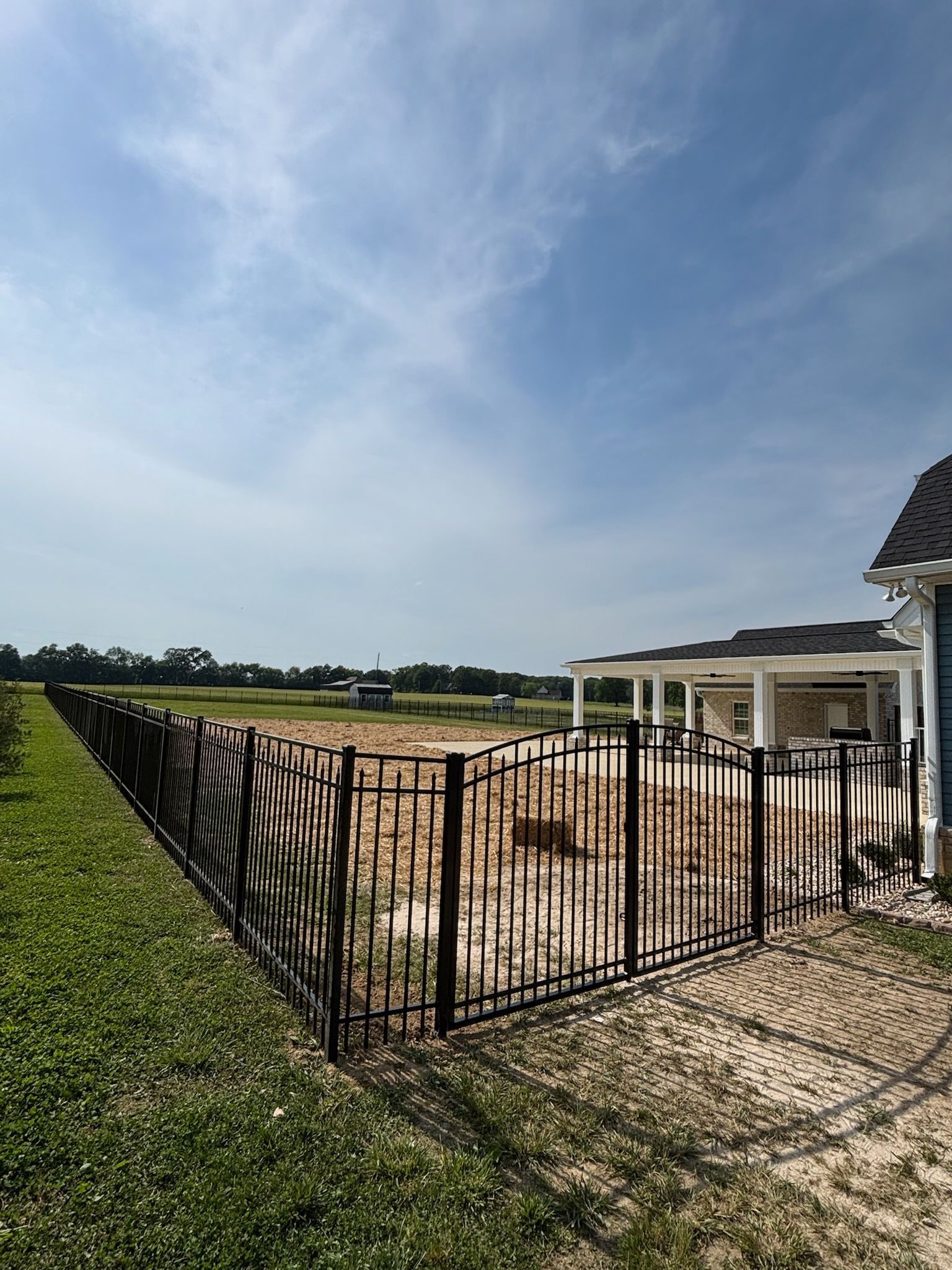 A black fence surrounds a grassy field in front of a house.