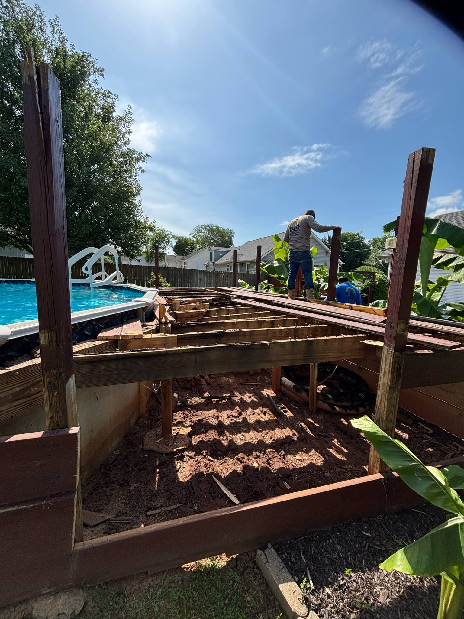 A man is working on a wooden deck next to a pool.