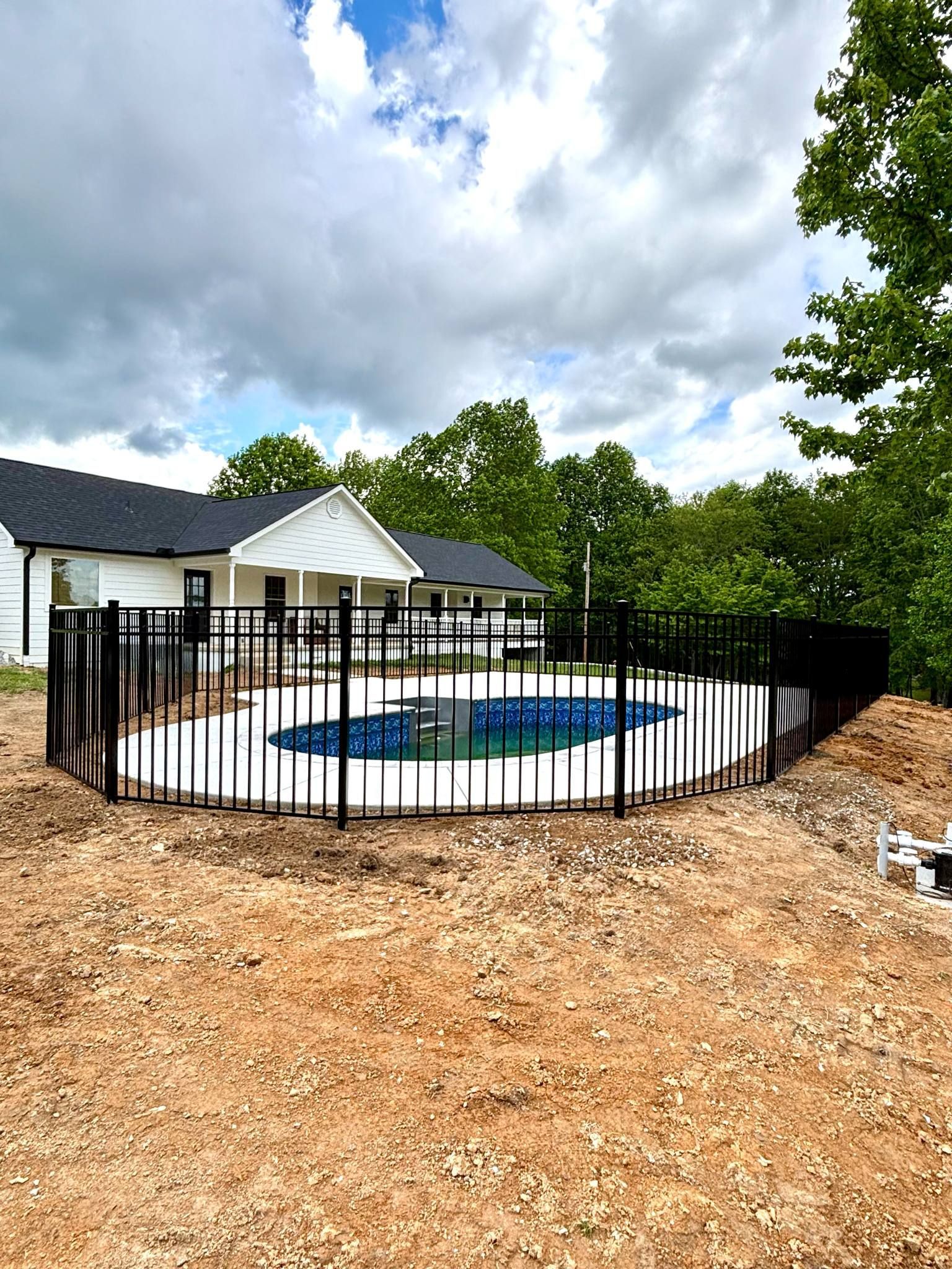 A large swimming pool is surrounded by a fence in front of a house.