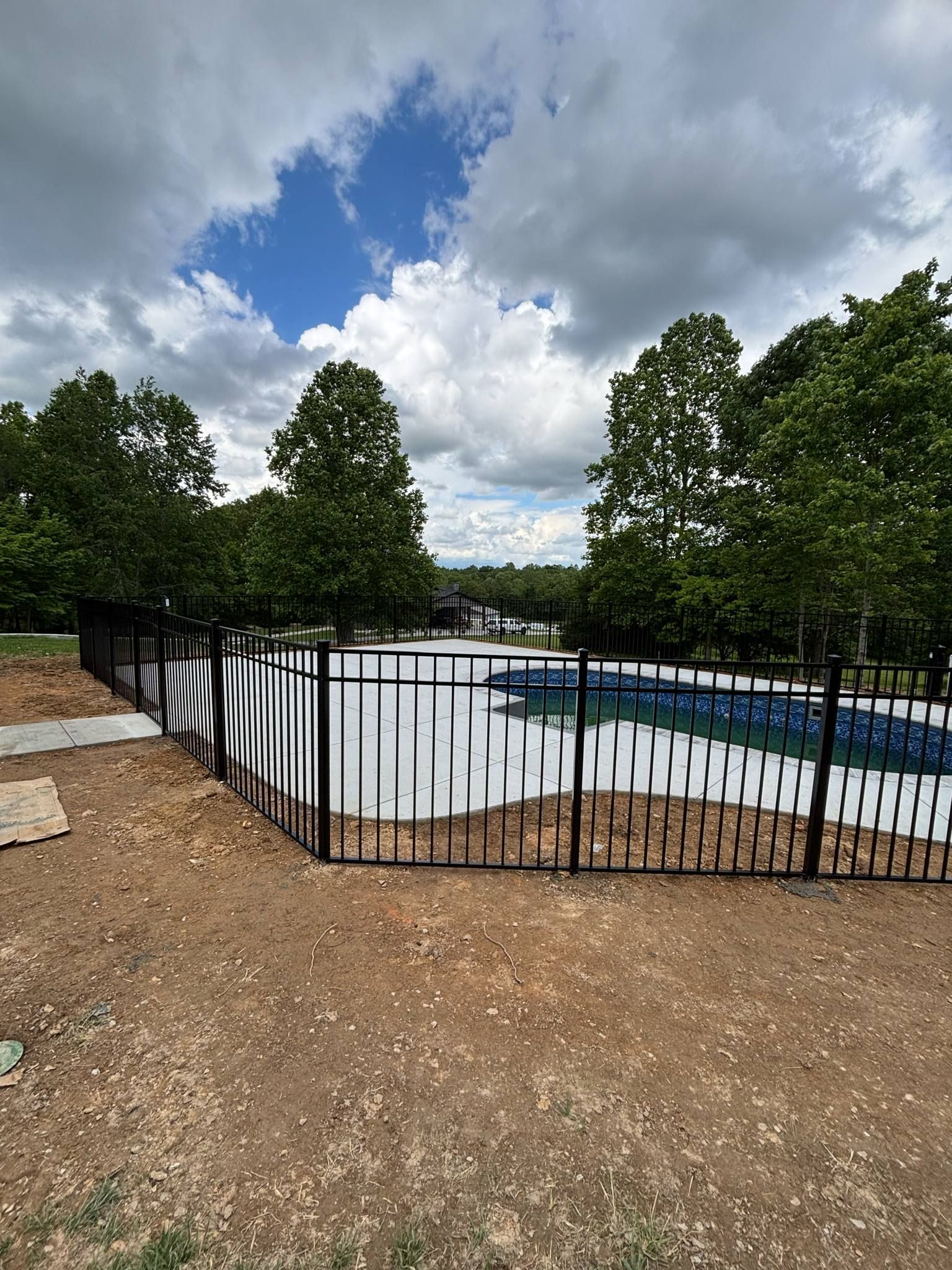 A large swimming pool is surrounded by a fence and trees.