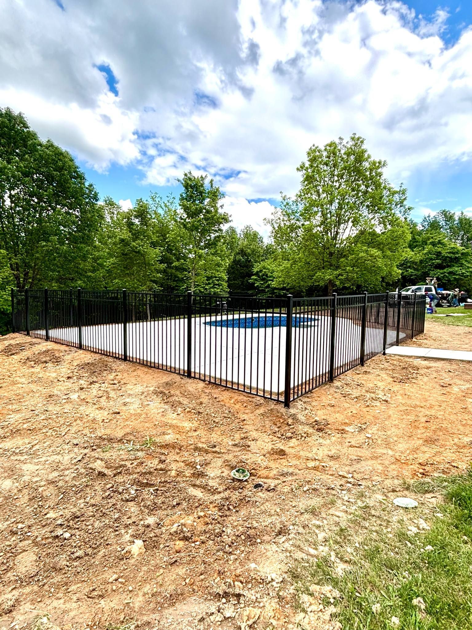 A black metal fence surrounds a swimming pool surrounded by trees.