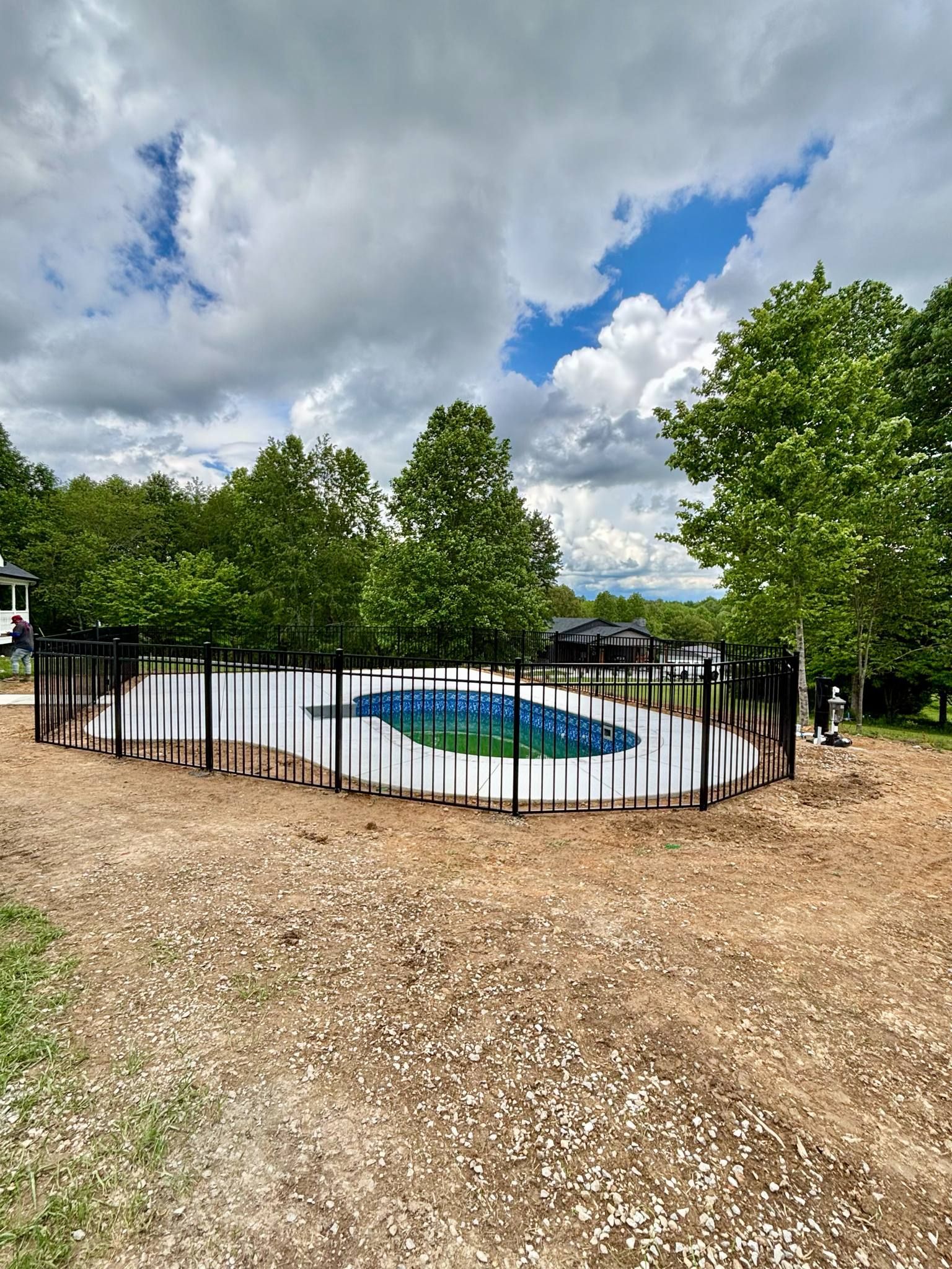 A large swimming pool surrounded by a fence and trees on a cloudy day.