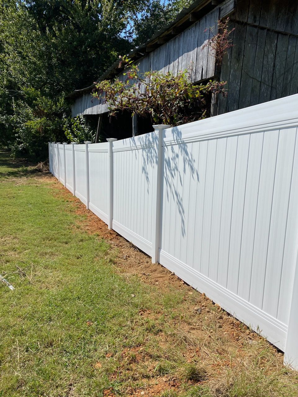 A white vinyl fence is sitting in the middle of a lush green yard.